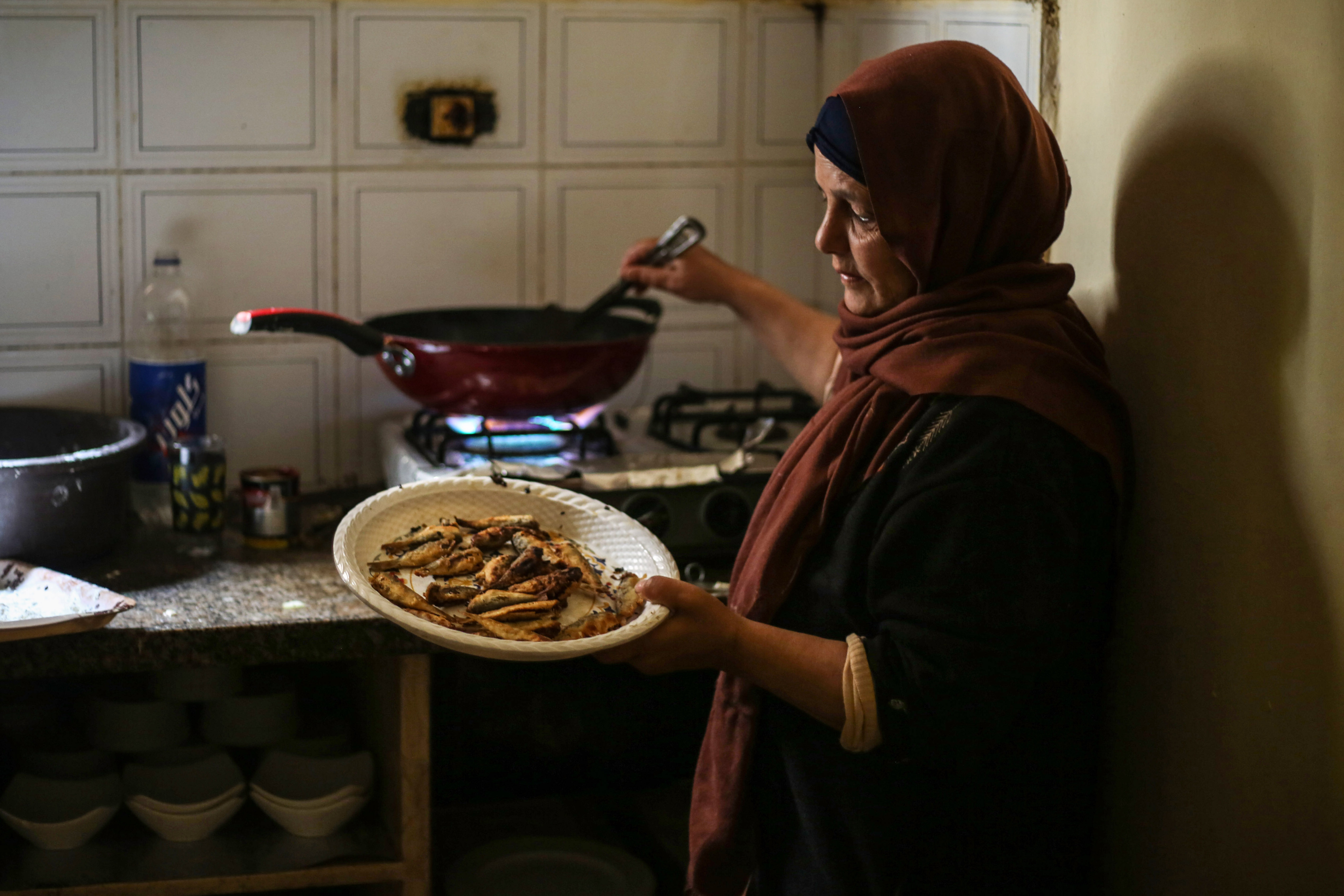 Khadr's mother stands by the stove lifting hot, freshly fried sardines out of a wok and onto a plate