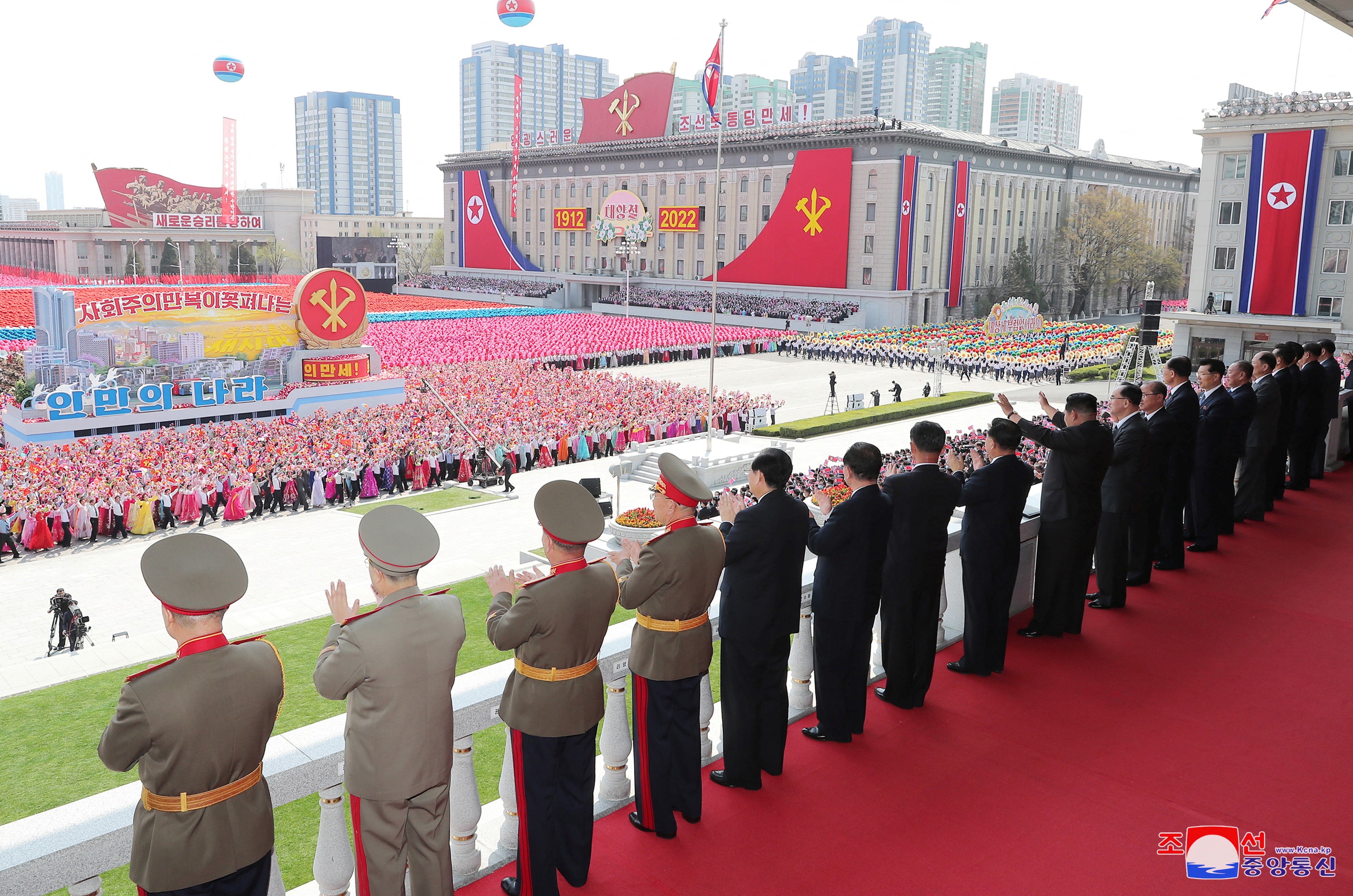 officials in miitary uniform line up on a balcony to watch the massive crowd in Kim Il Sung Square