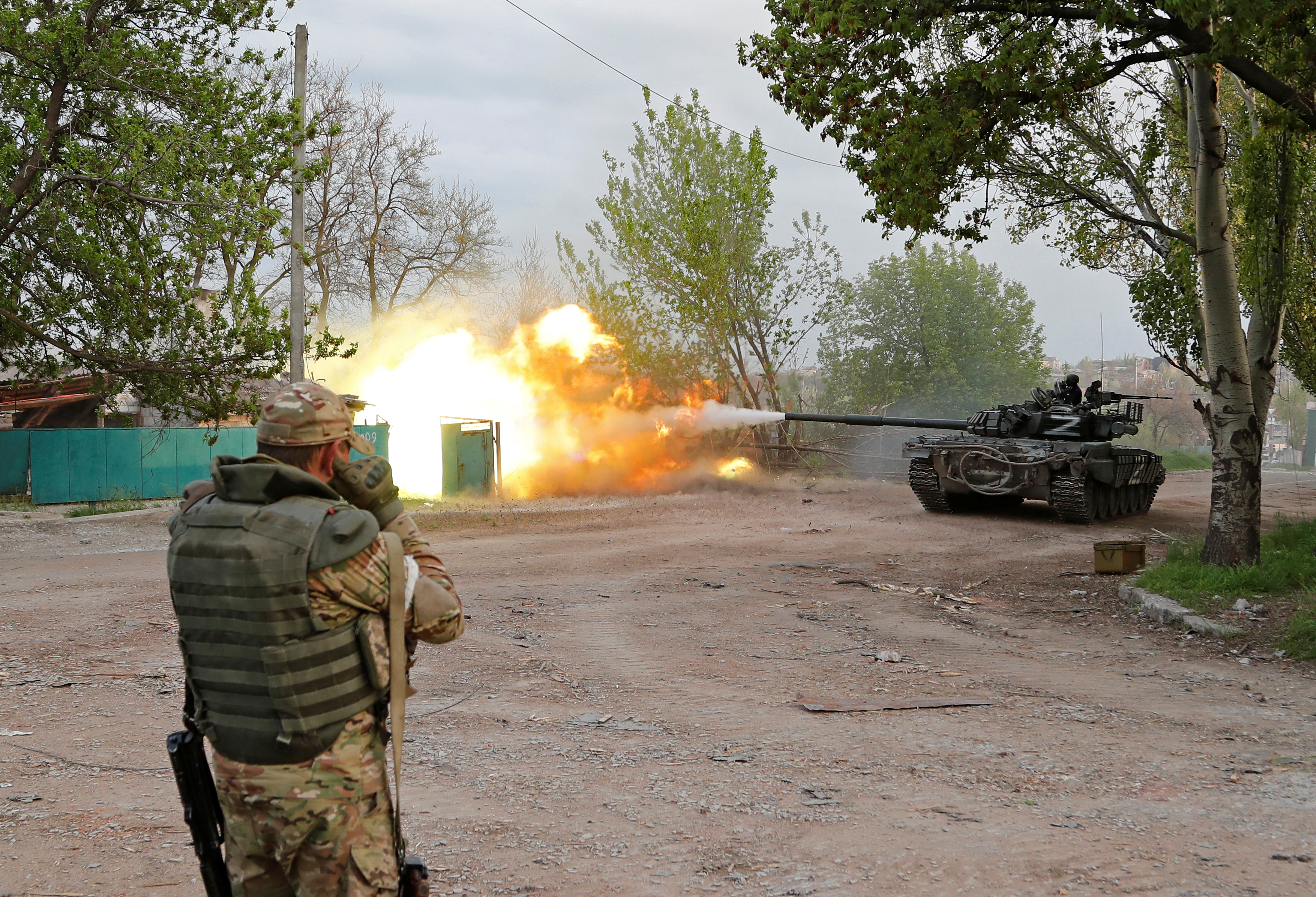 A soldier with his back to the camera raises his weapon as a tank of pro-Russian forces advances near the Azovstal steel works