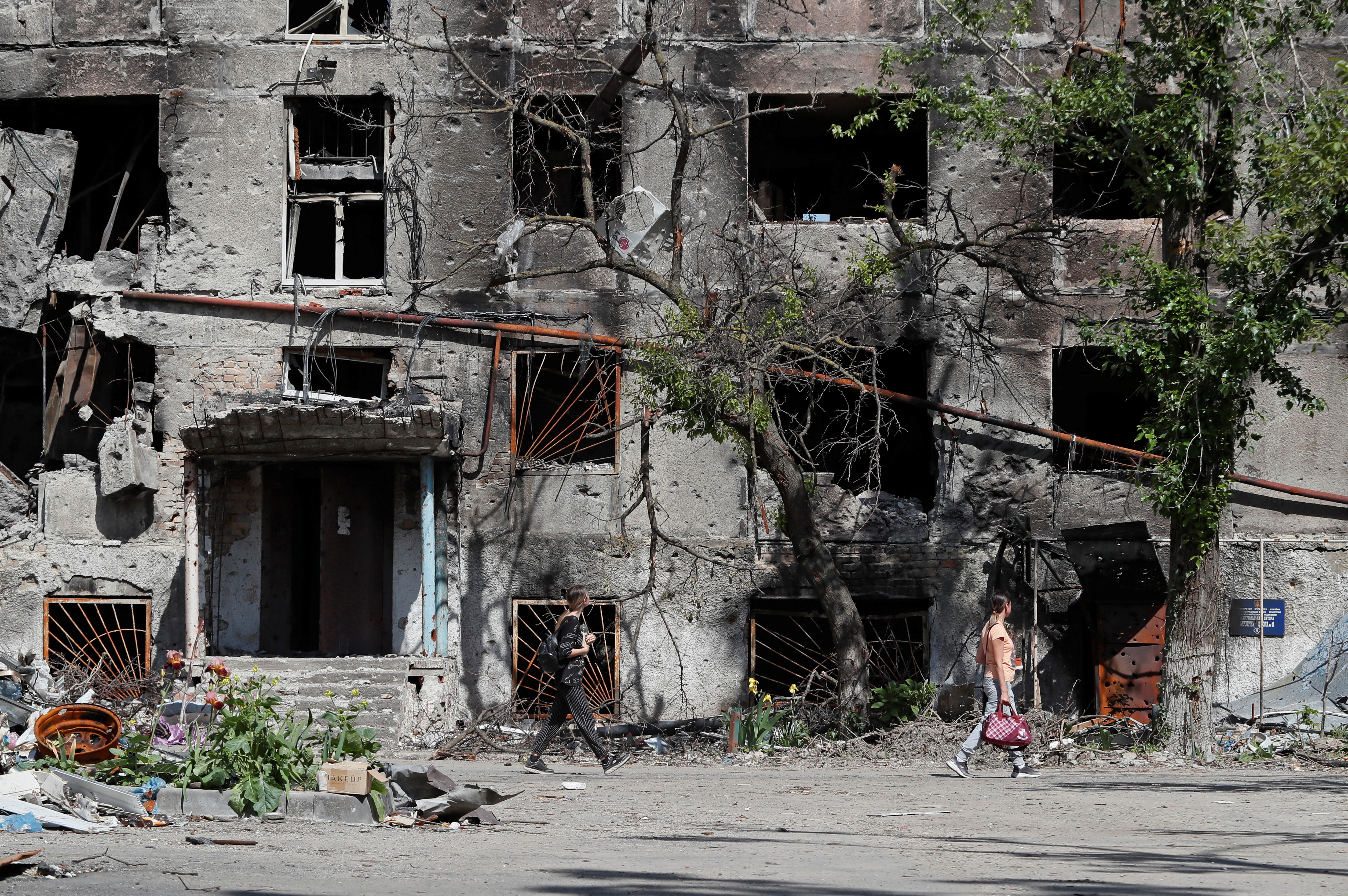 Destroyed buildings in Mariupol, Some peple are walking past.