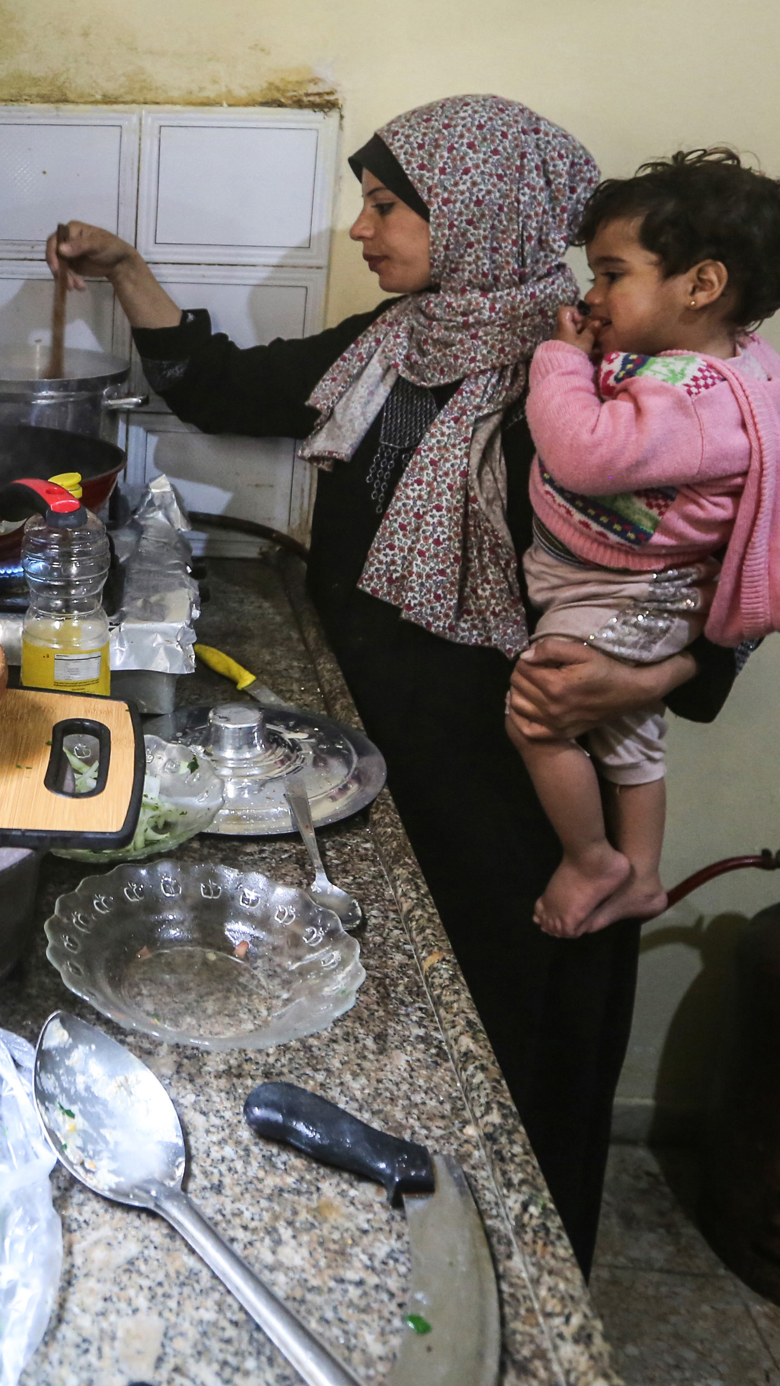 Madelyn holds Sandy in one arm as she stirs a pot on the stove