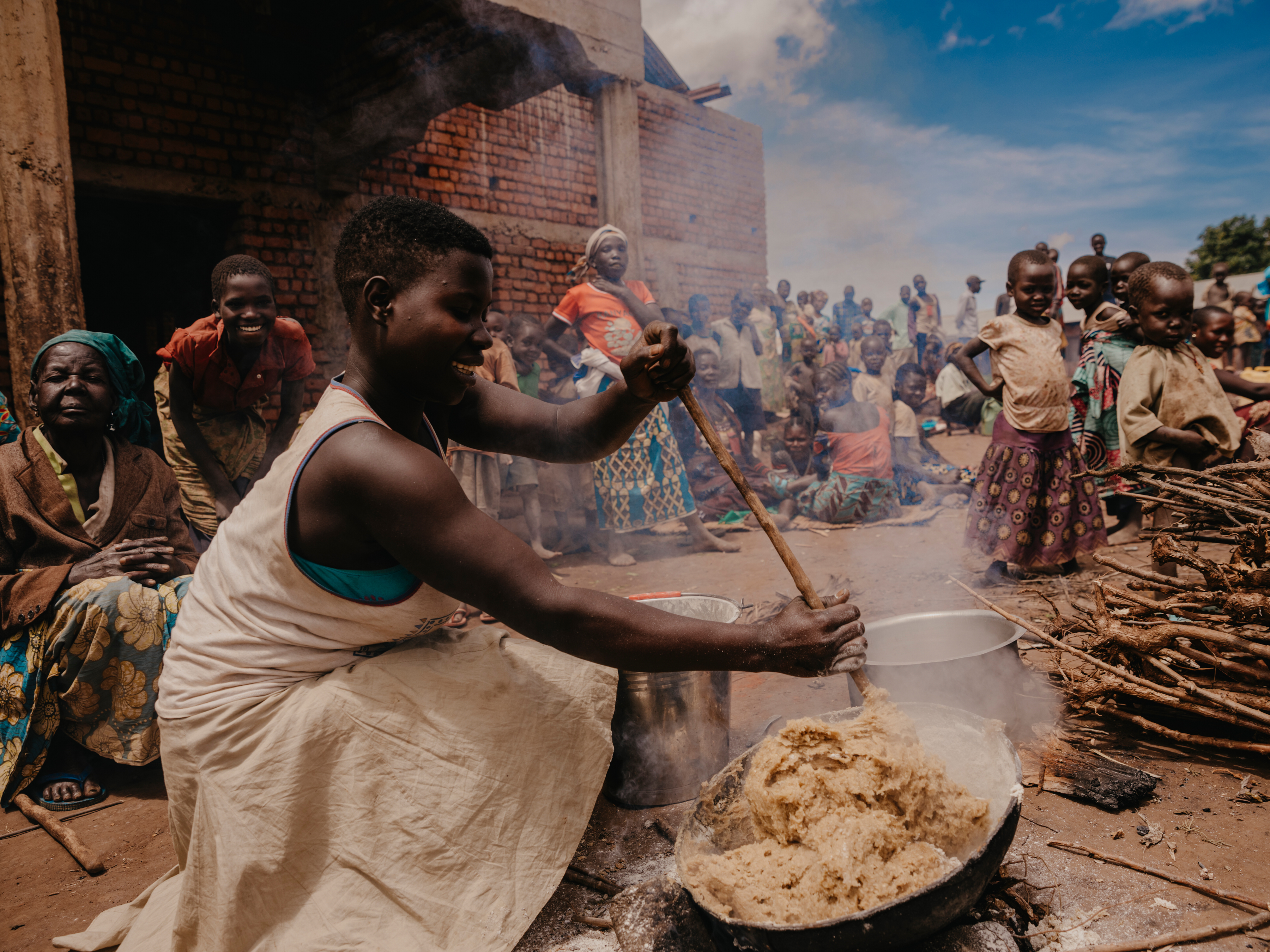 A woman cooks casava, a filling but not nutritious root, near a church in Djukot, Ituri Food prices are soaring, partly due to the war in Ukraine. Since March 2022, the cost of sugar and cooking oil has risen by 50 per cent, bread by 20 per cent and rice by 11 per cent, posing a huge challenge in a country experiencing historic levels of hunger. 2.2 million people in Ituri province are going hungry – a number estimated to increase this year.