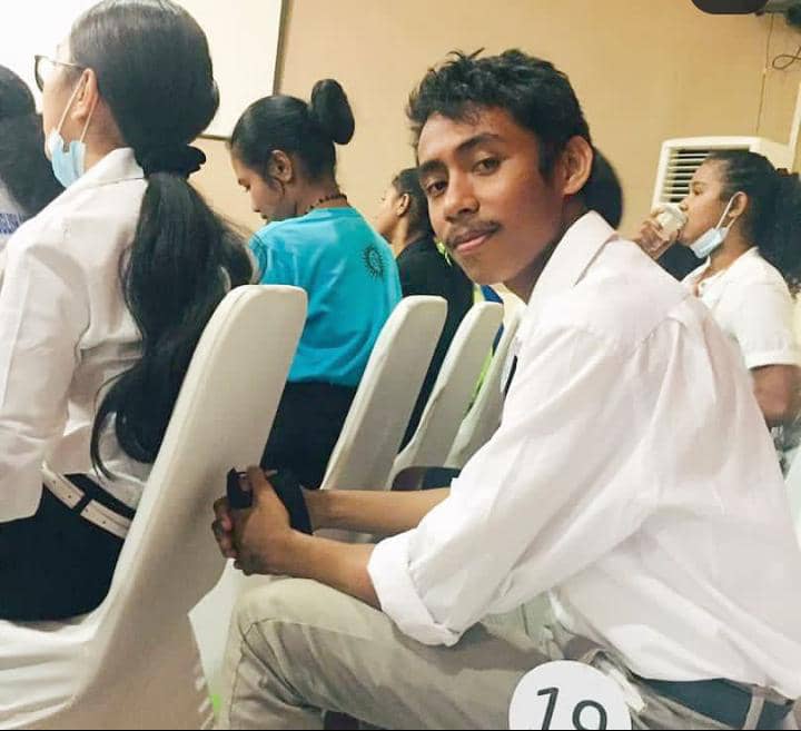 Levilito Das Neves Baptista in white short and grey trousers sitting on a chair at at a function