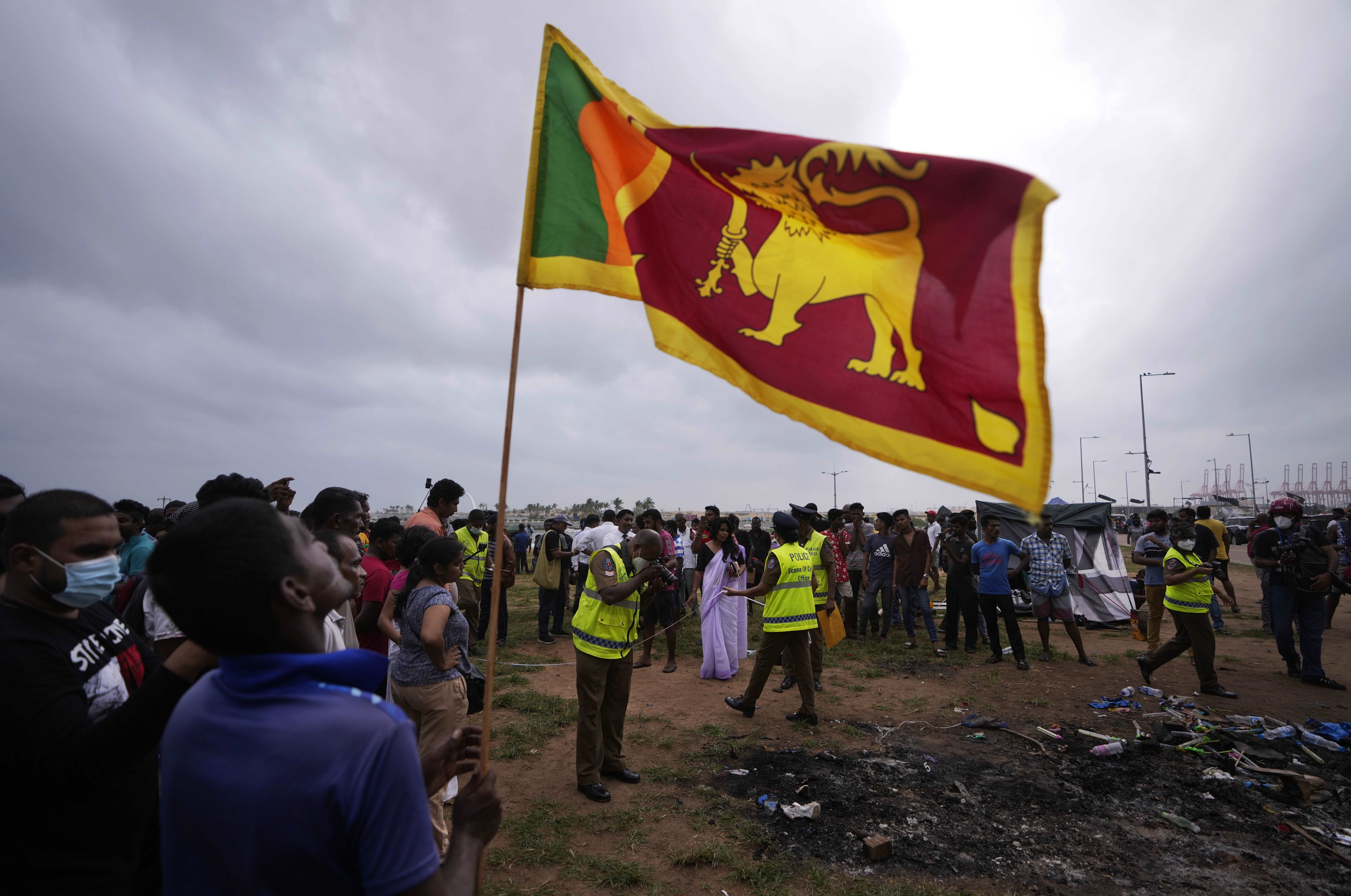 A Sri Lankan man holds a national flag as police officers conduct investigations into aftermath of clashes between government supporters and anti government protesters in Colombo, Sri Lanka on May 10.