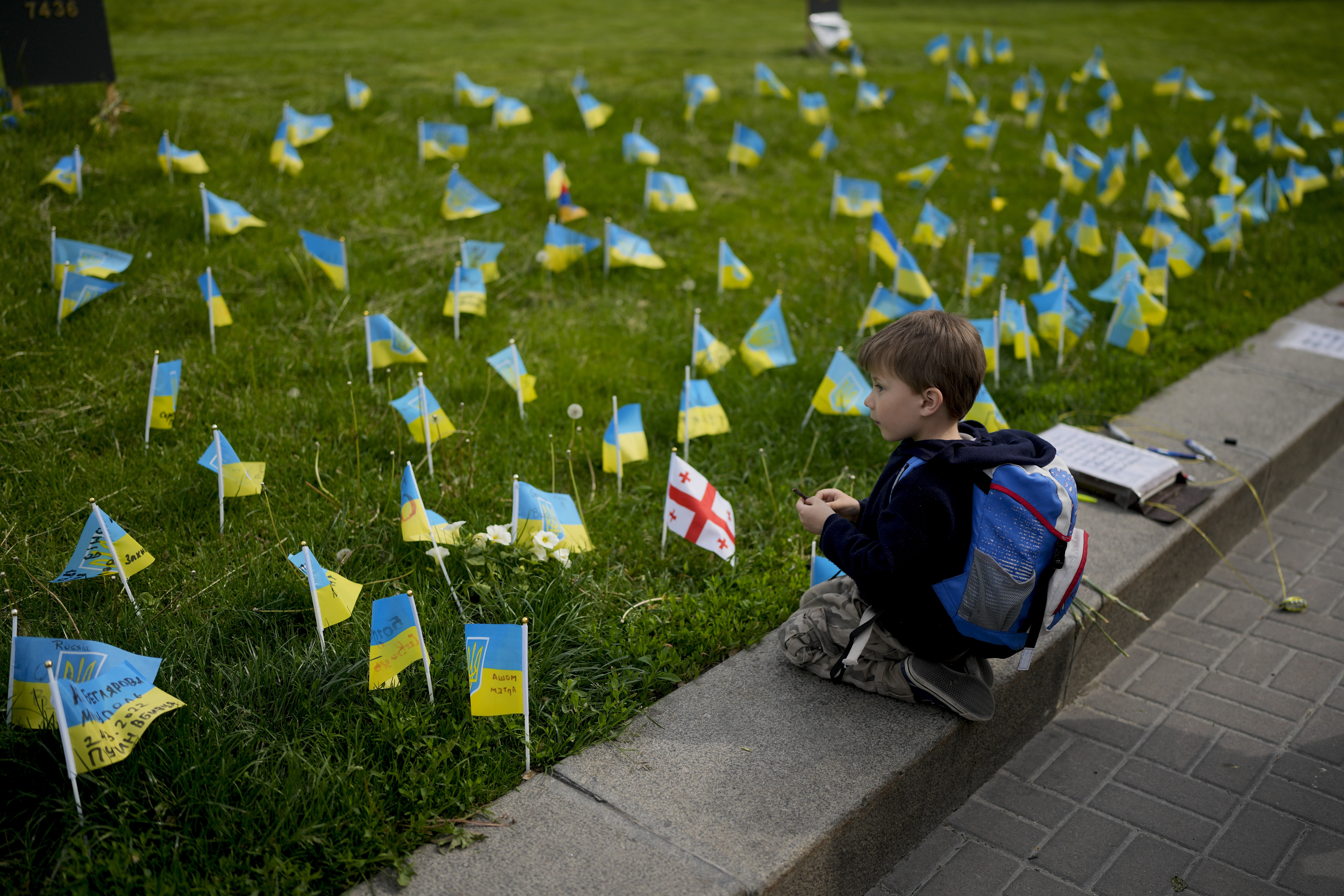 A boy watches flags honoring soldiers killed fighting Russian troops in downtown Kyiv, Ukraine, Monday, May 23, 2022