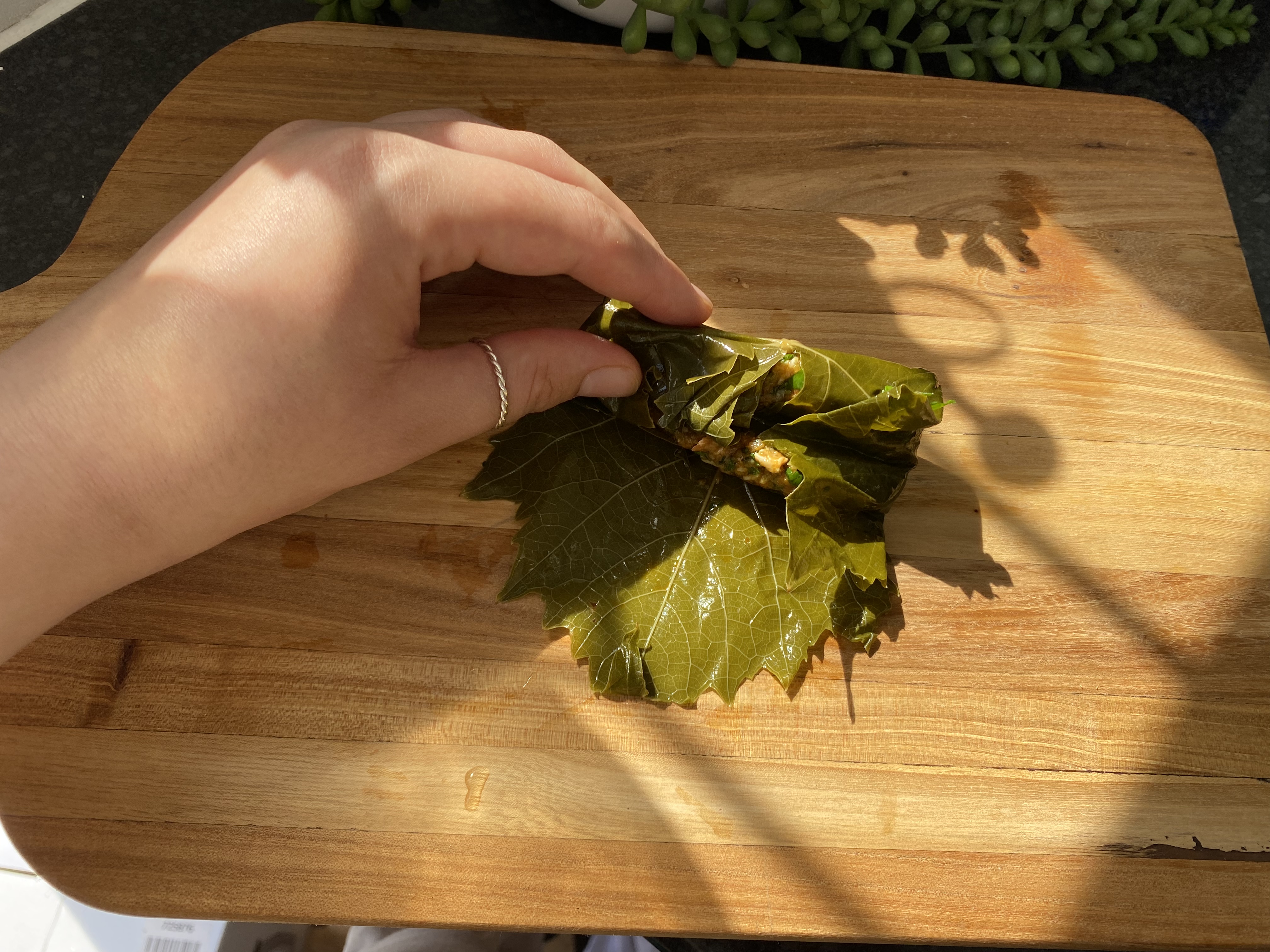 A hand is seen rolling rice mixed with spiced mince in a grape leaf