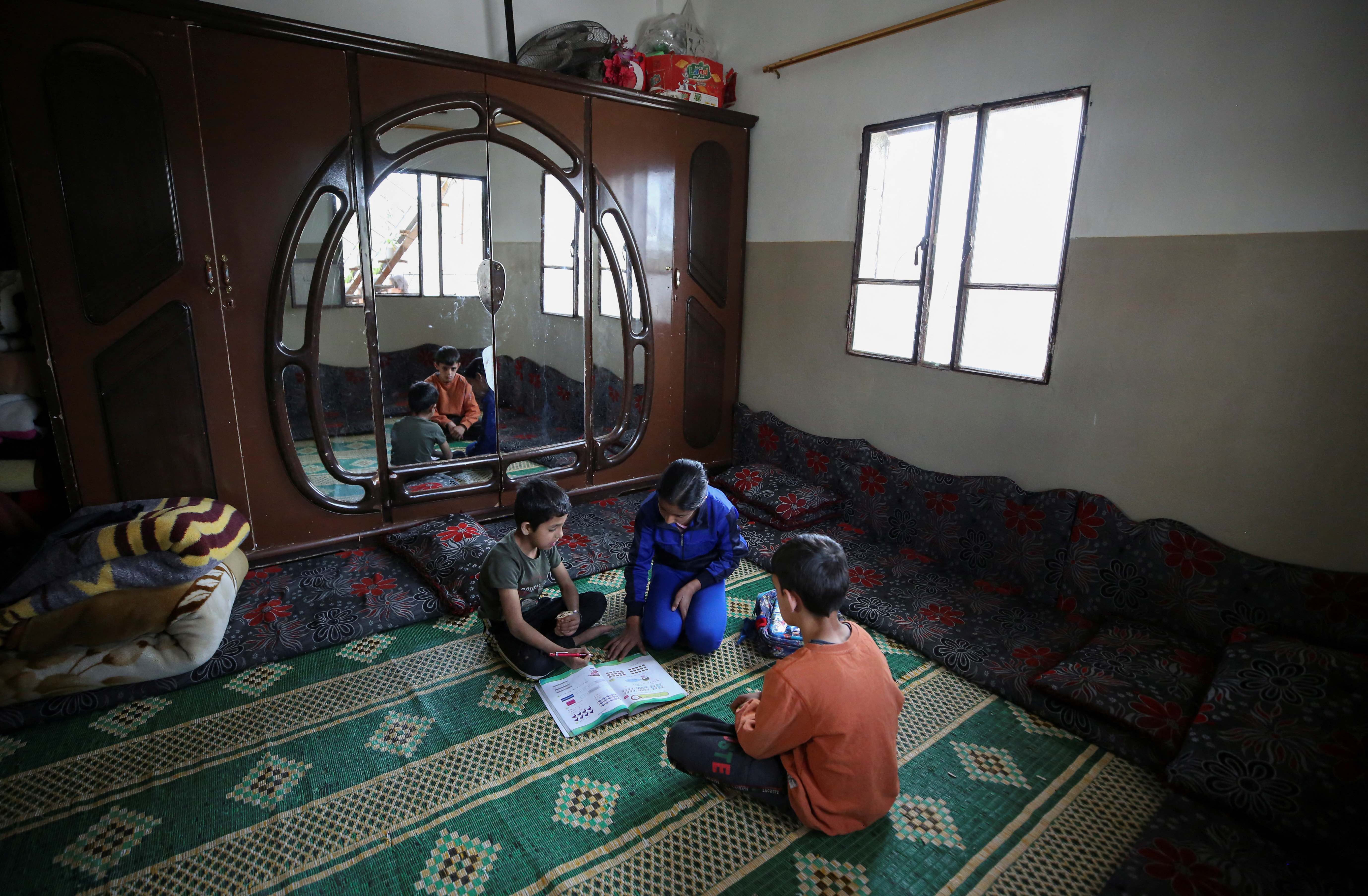 A girl helps her younger brother with his homework at their family home in Salamiyah, a town in the western province of Hama, Syria