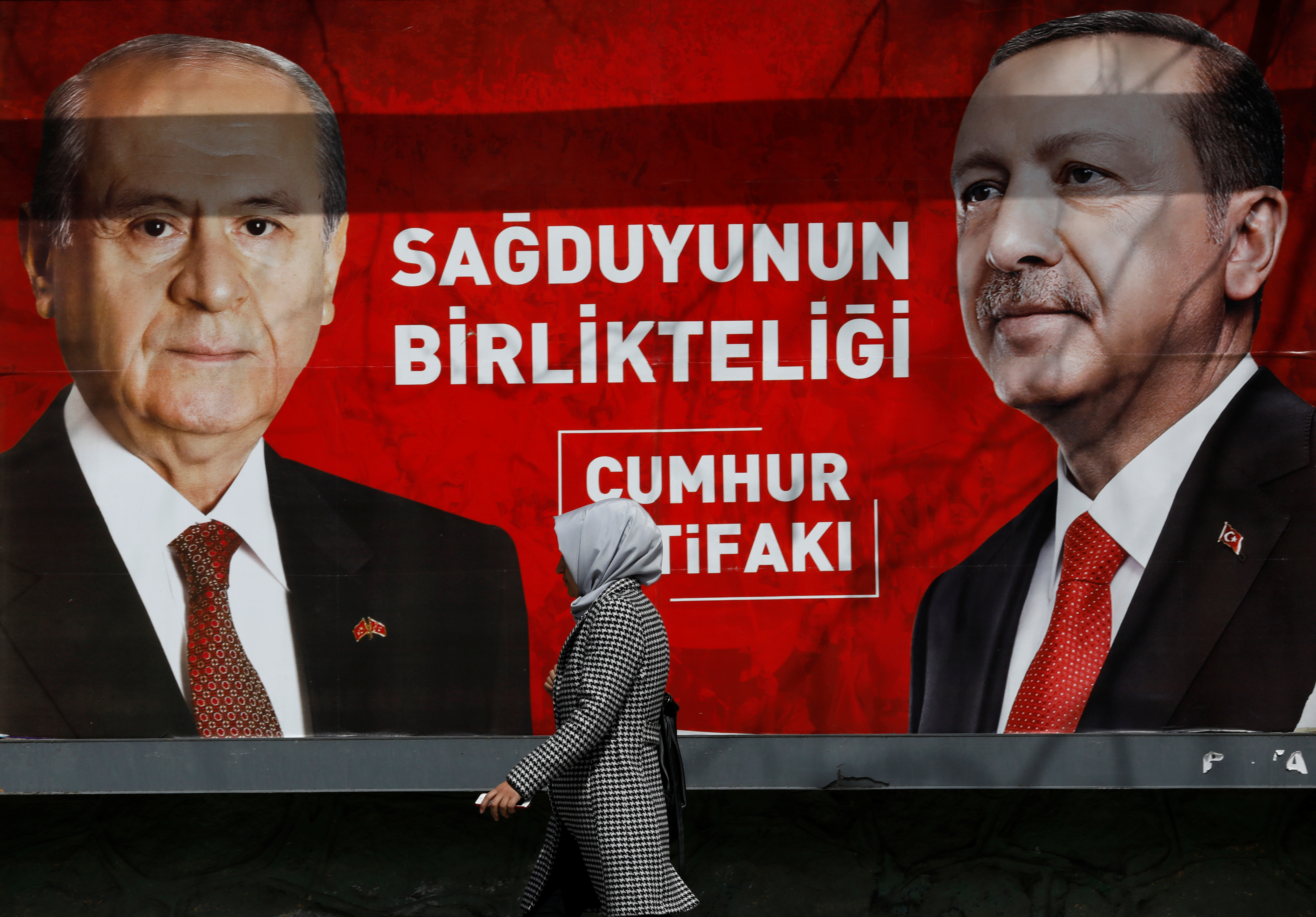 Woman walks past a billboard featuring Turkish President Erdogan and MHP leader Bahceli