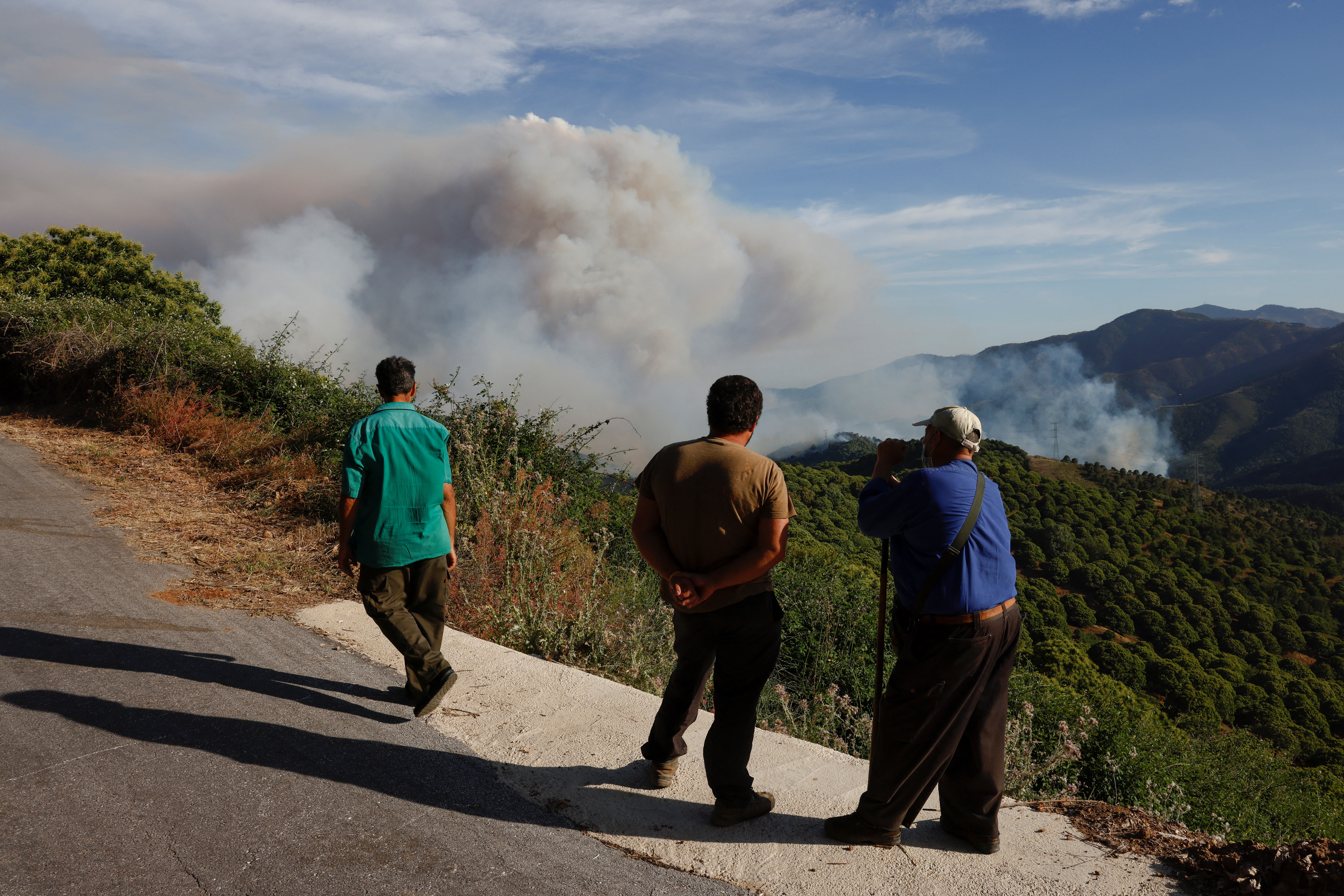 People watch as smoke billows, as a forest fire breaks out in Pujerra,