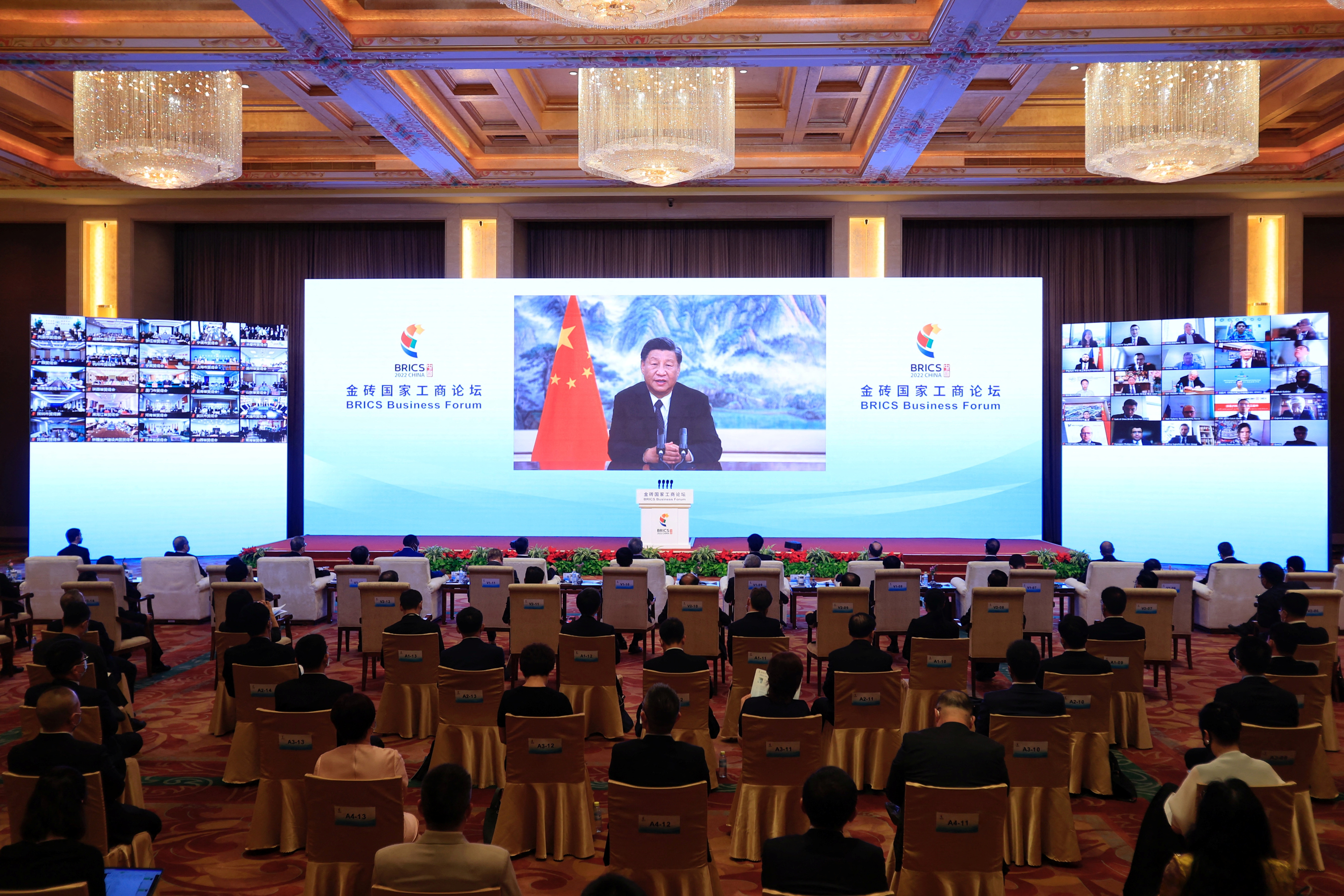 Xi Jinping speaks from a large screen to a virtual forum in Beijing with the audience sitting spaced apart on individual chairs because of COVID-19