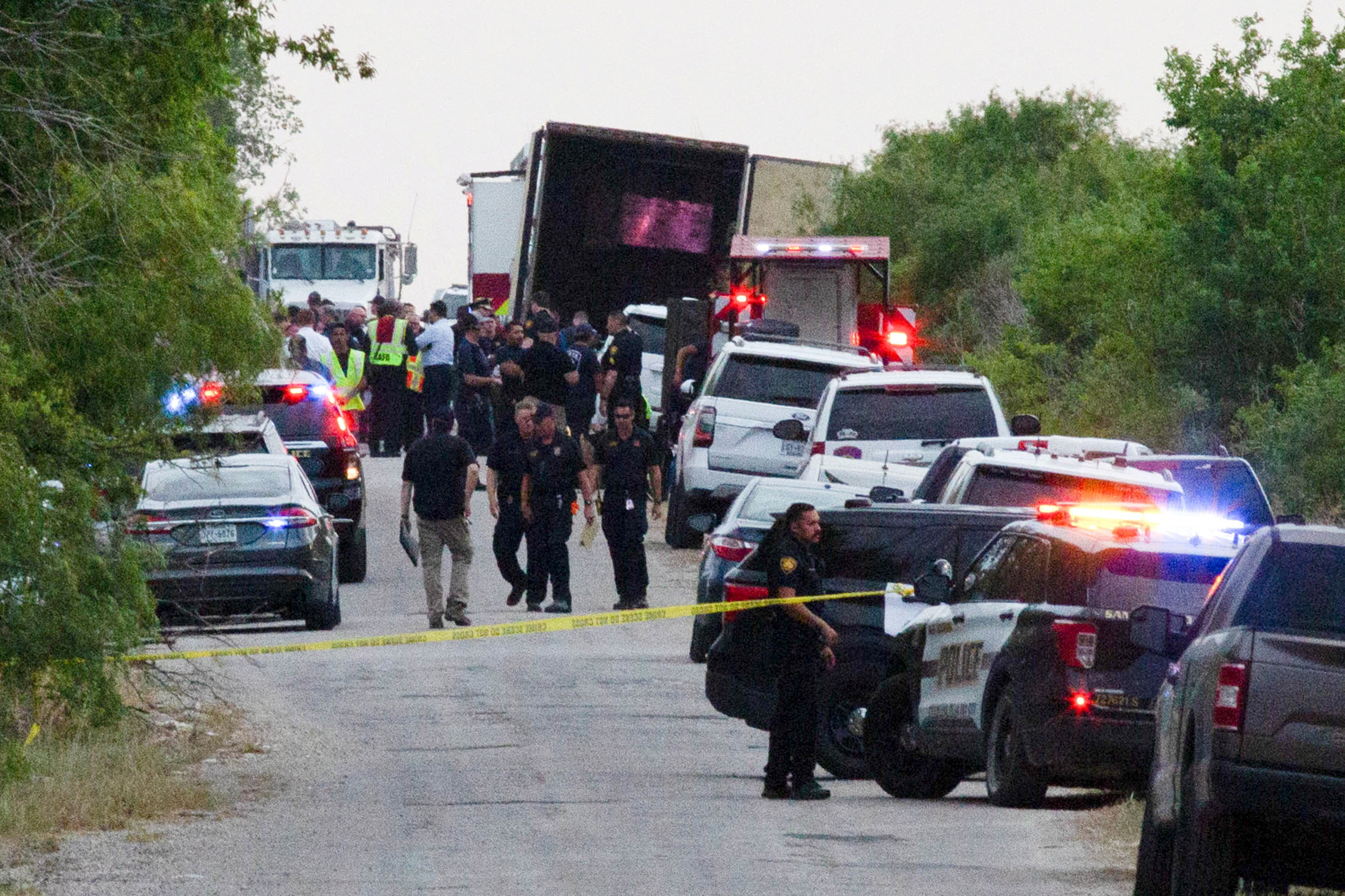 Law enforcement officers work around tractor-trailer with its doors ajar.