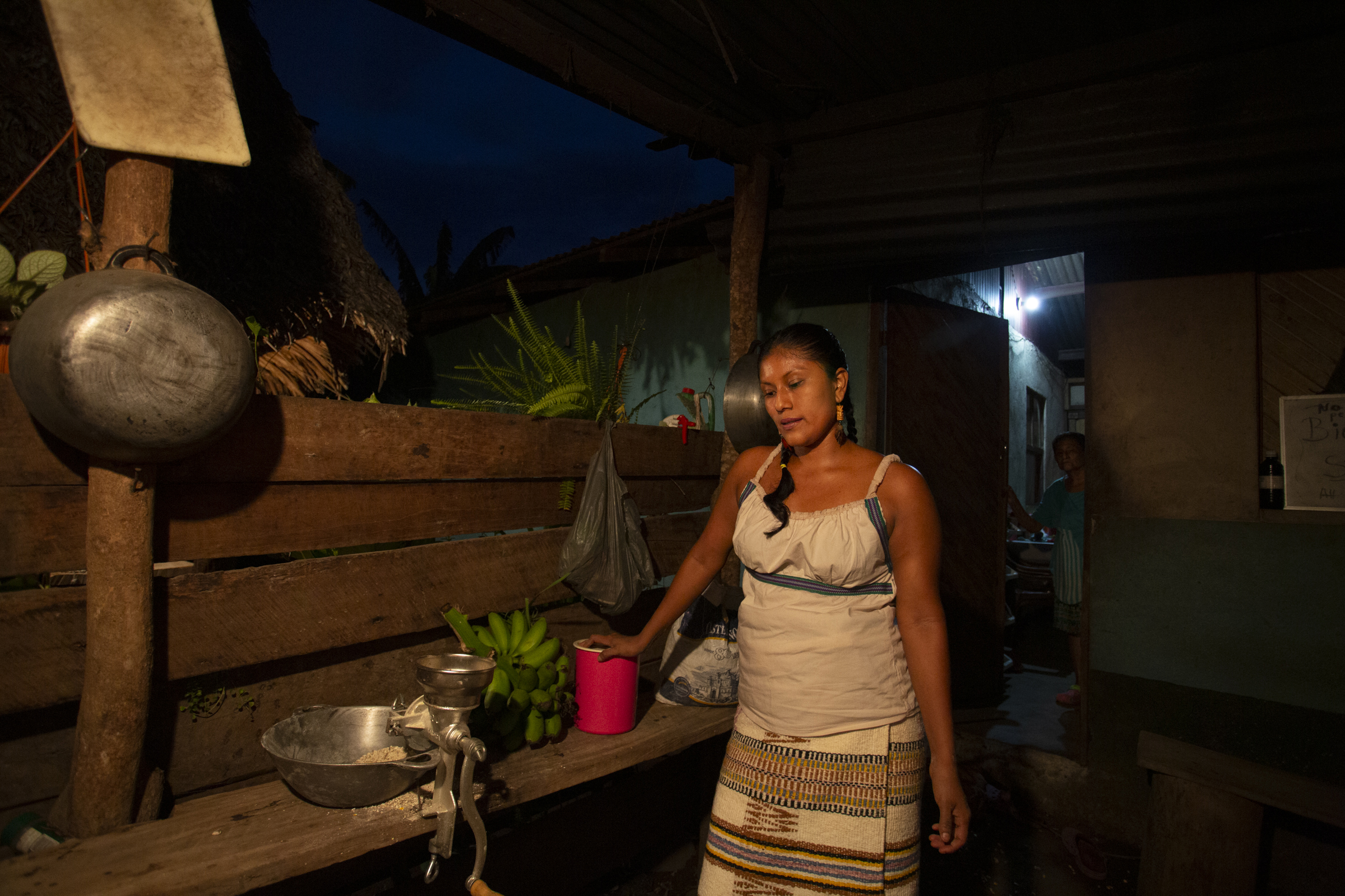 A photo of Cecilia Leyva, 35, leaning on a wooden table with a woman standing in the back near an open door.