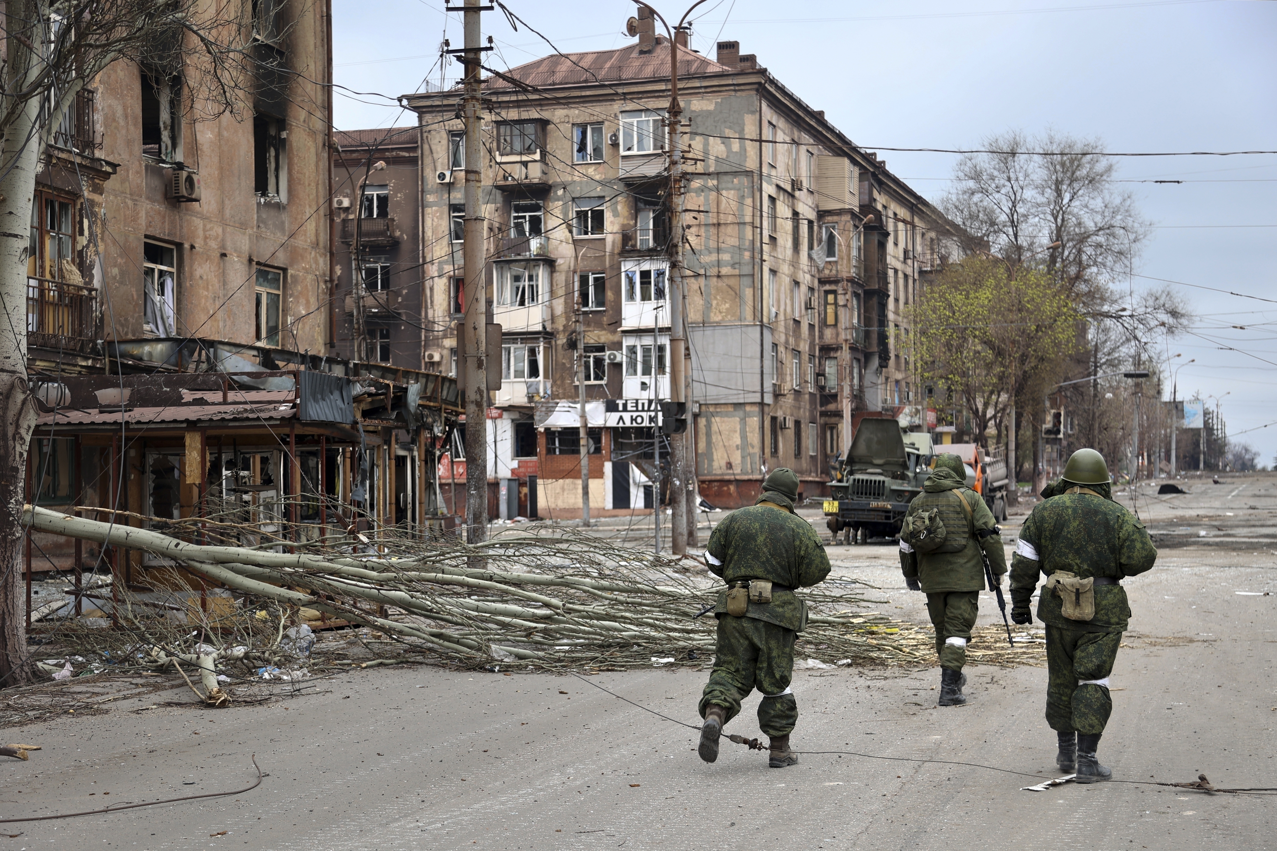 FILE - Servicemen of the militia from the Donetsk People's Republic walk past damaged apartment buildings near the Illich Iron & Steel Works Metallurgical Plant, the second-largest metallurgical enterprise in Ukraine, in an area controlled by Russian-backed separatist forces in Mariupol, Ukraine, Saturday, April 16, 2022. Mariupol, which is part of the industrial region in eastern Ukraine known as the Donbas, has been a key objective for Russia since the start of the Feb. 24 invasion