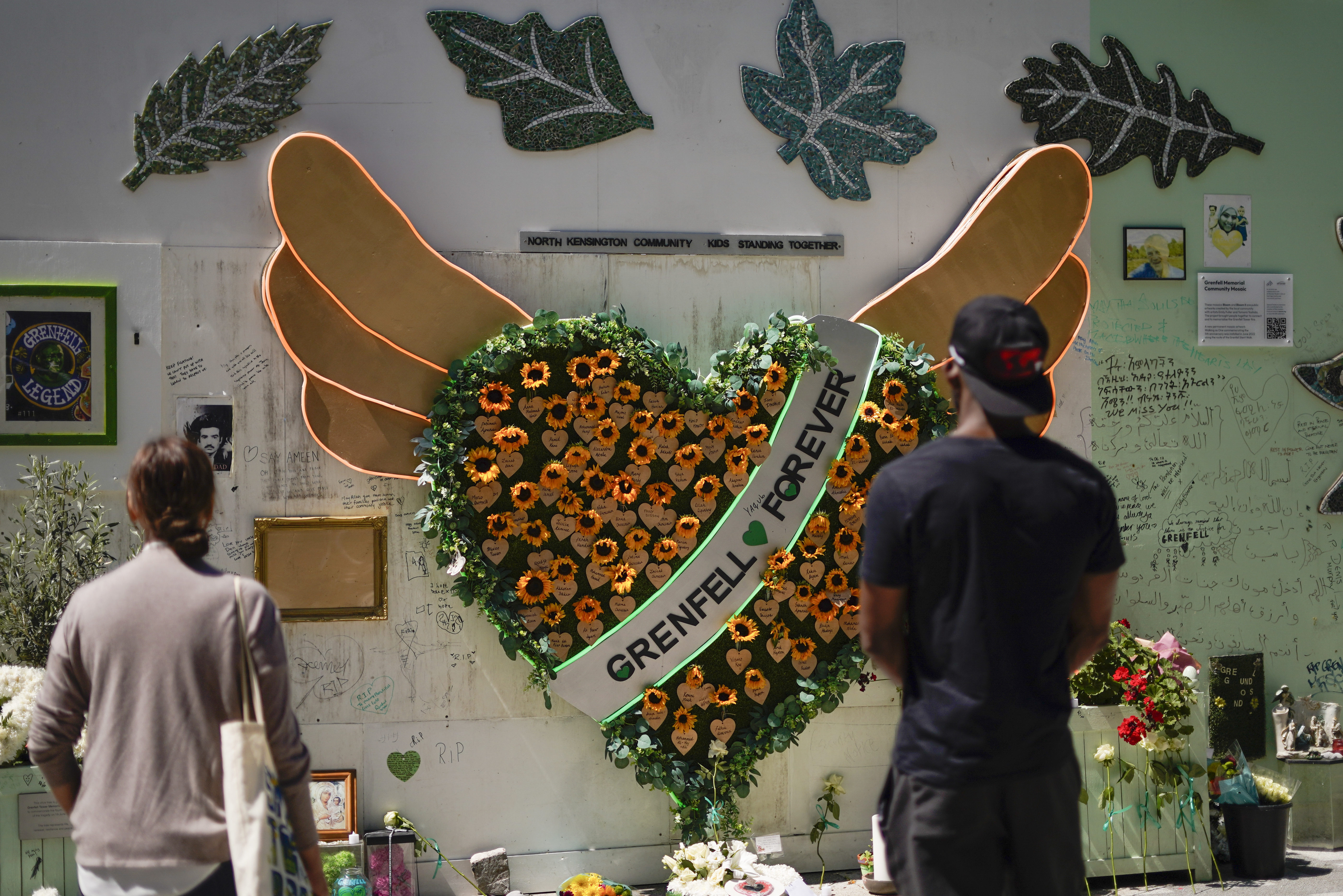 People observe the memorial, near to the remains of the Grenfell Tower