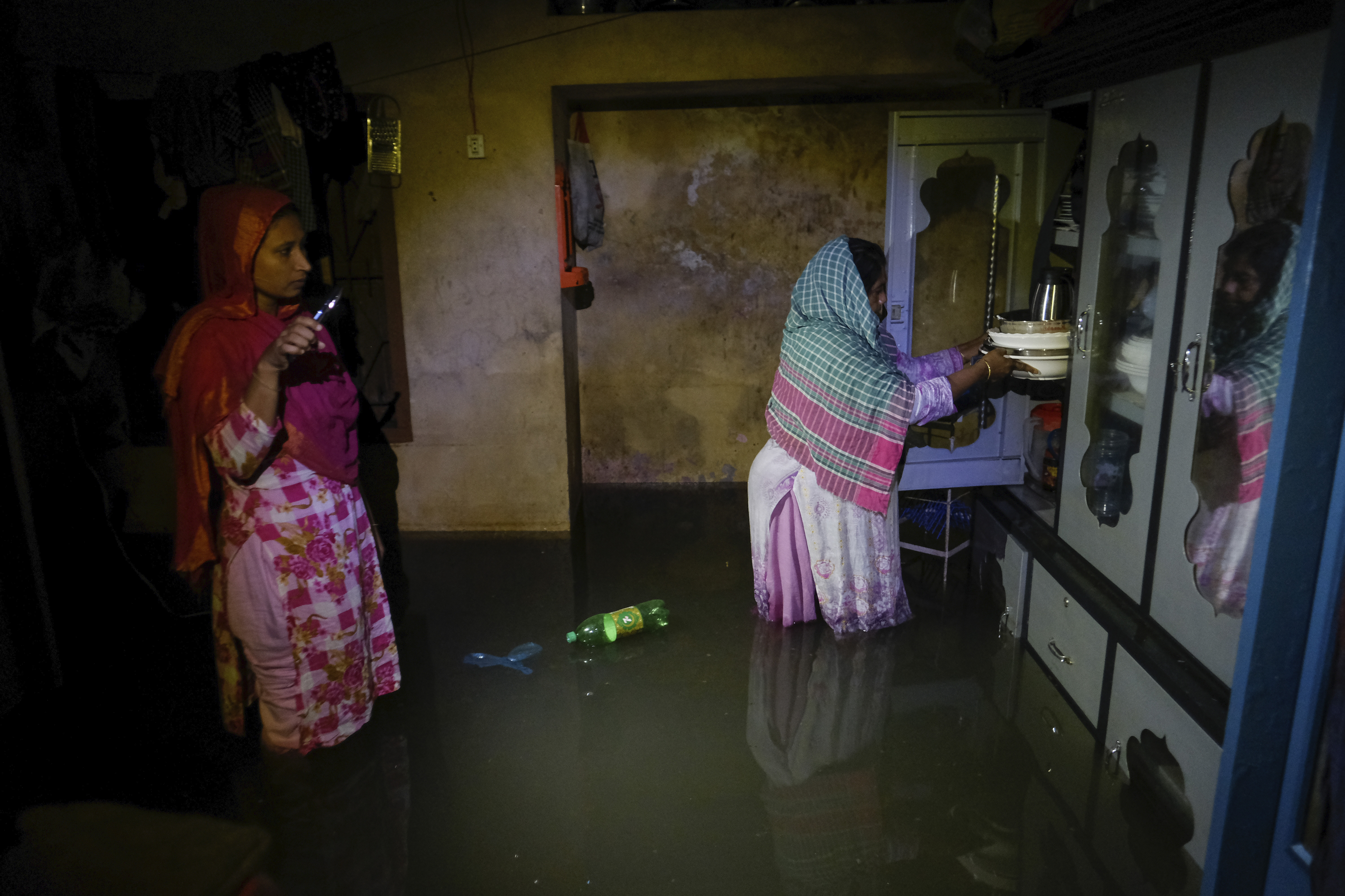 Two women stand inside a flooded home in Sylhet