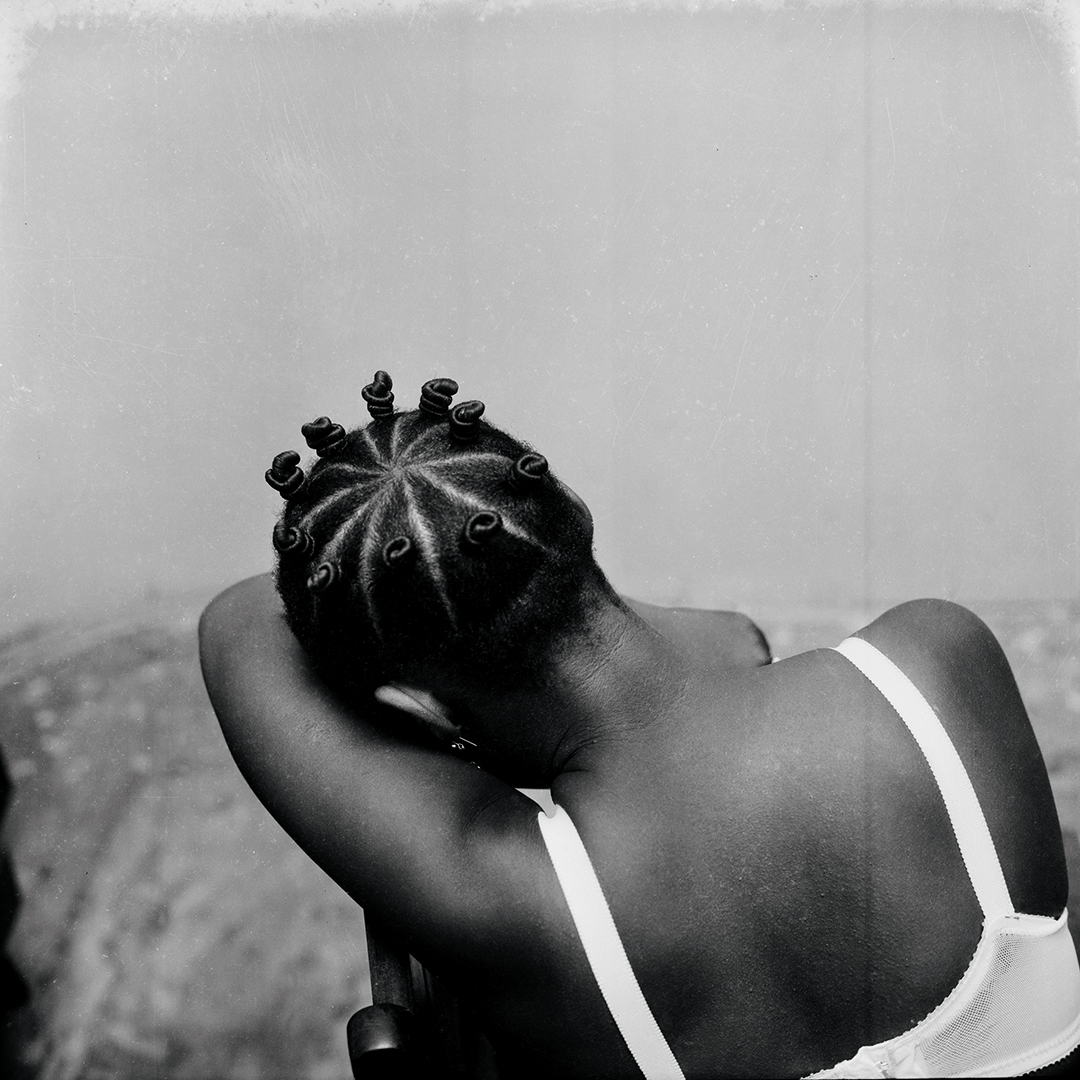 A photo of a woman from the back, with her head down in one of her arms.