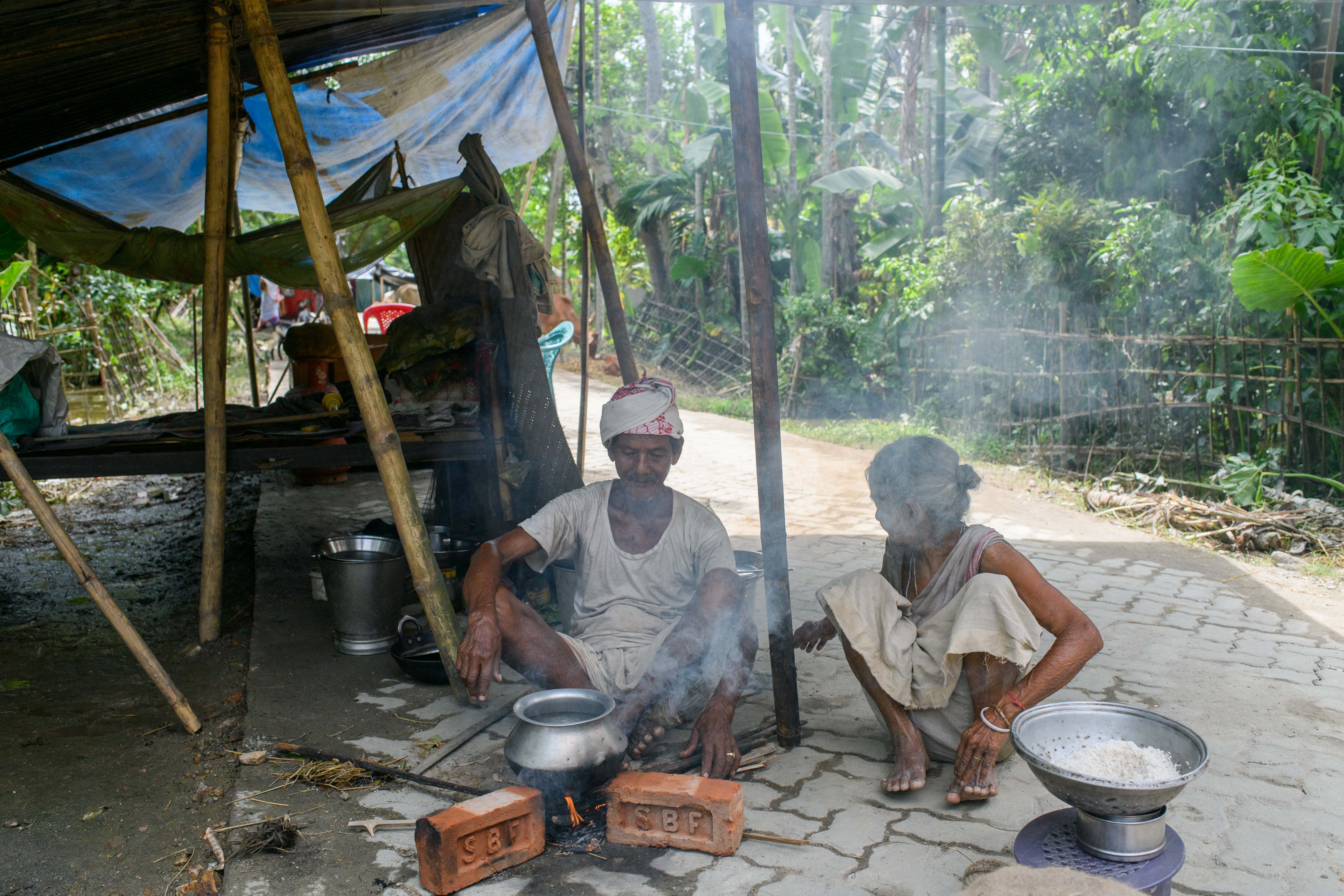 Both in their 80s, Lotibor Deka watches as his wife Junaki Deka makes lunch with the rice and lentils got as flood relief in their tent in Rupahitoli village