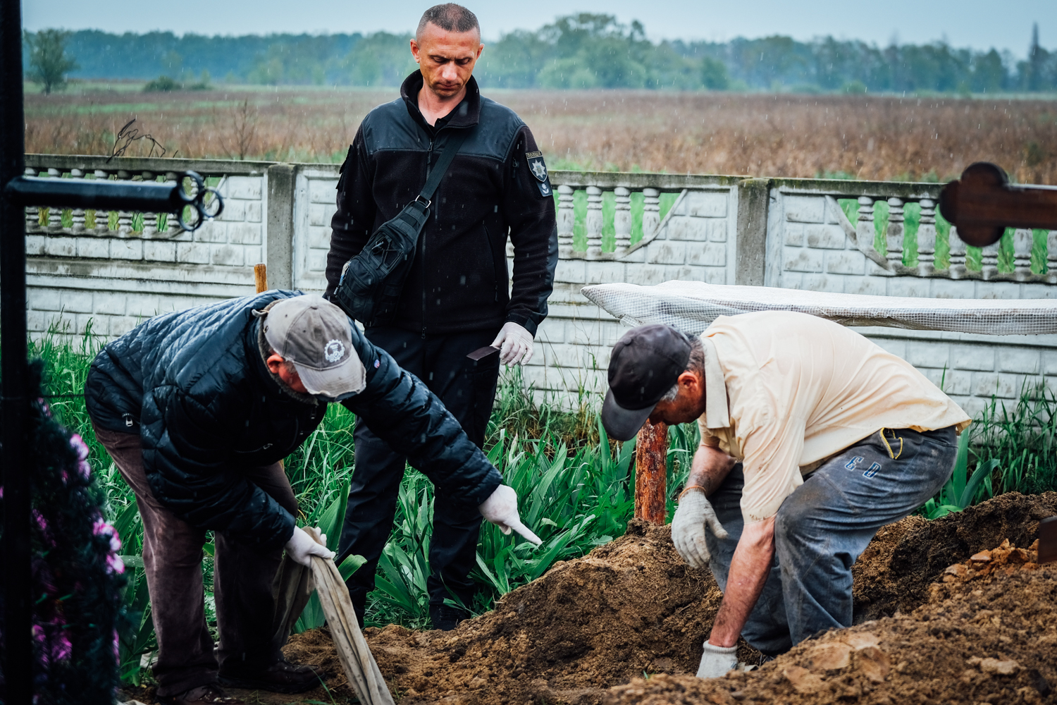 A photo of three people, one standing in the middle and two on either side of him kneeling on the ground.