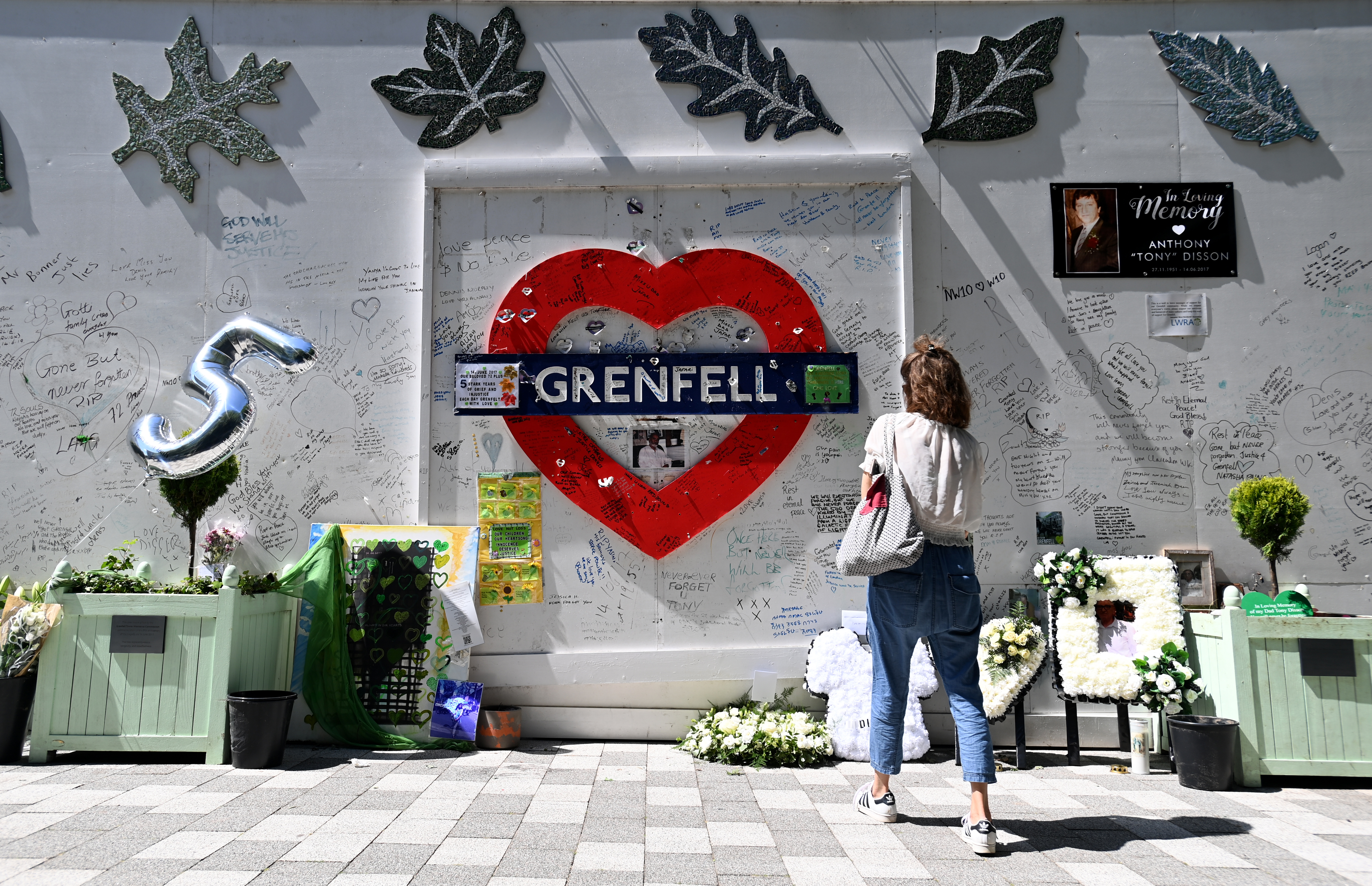A woman stands before the Grenfell Tower Memorial Wall near the Grenfell Tower