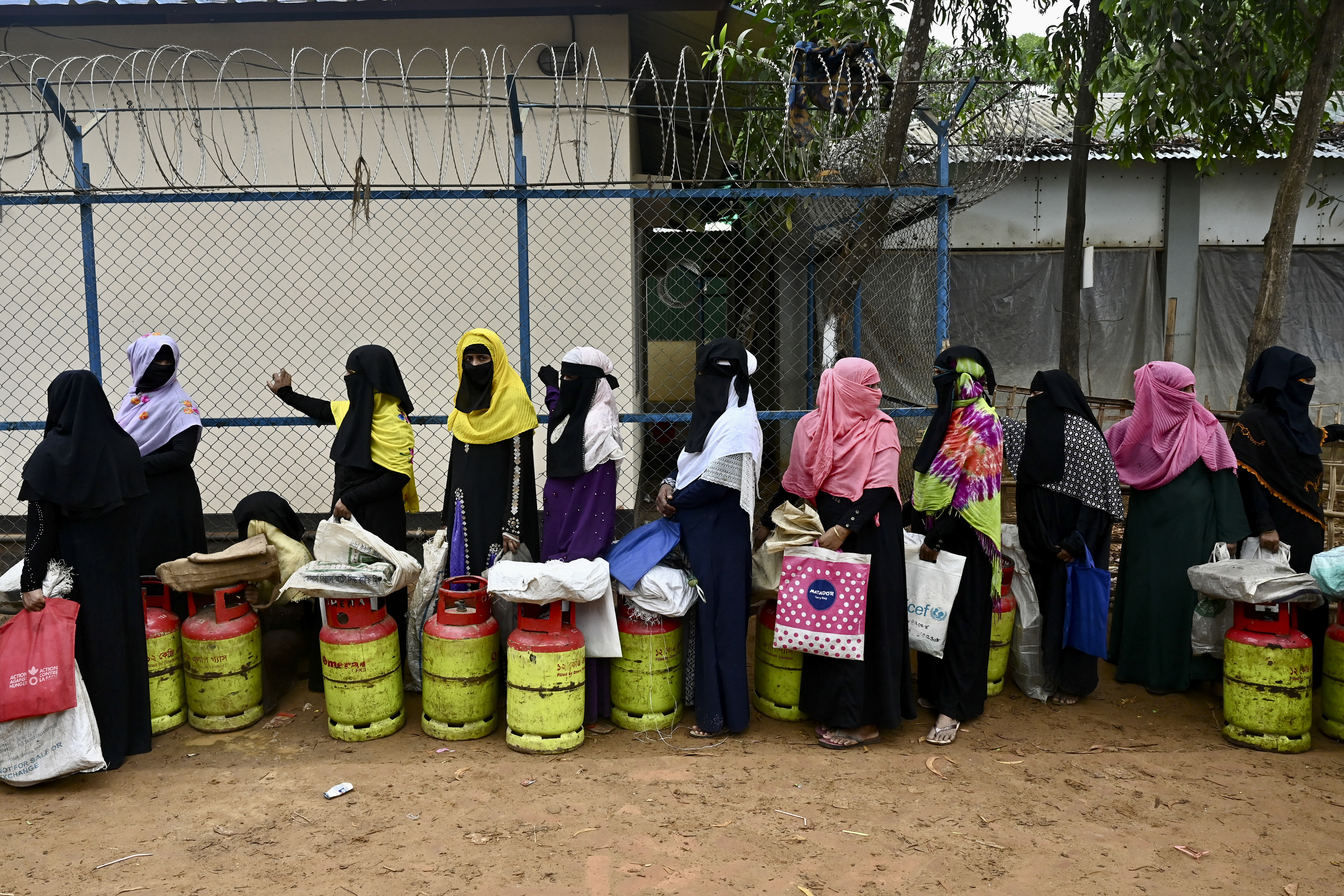 Rohingya women queue for gas canisters against a wire fence topped with barbed wire at the Kutupalong refugee camp in Bangladesh.