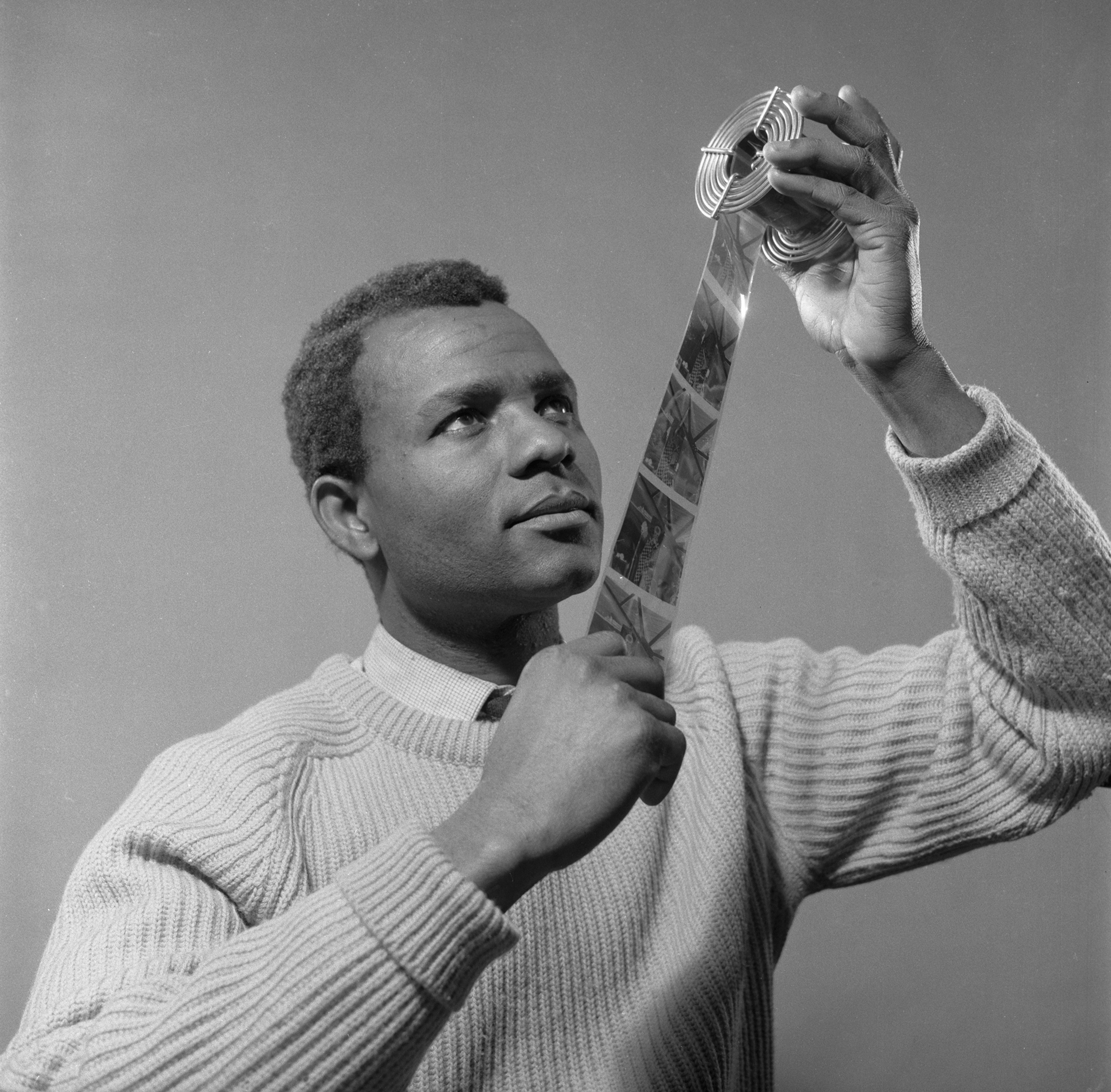 Photo of a young James Barnor looking at a film strip