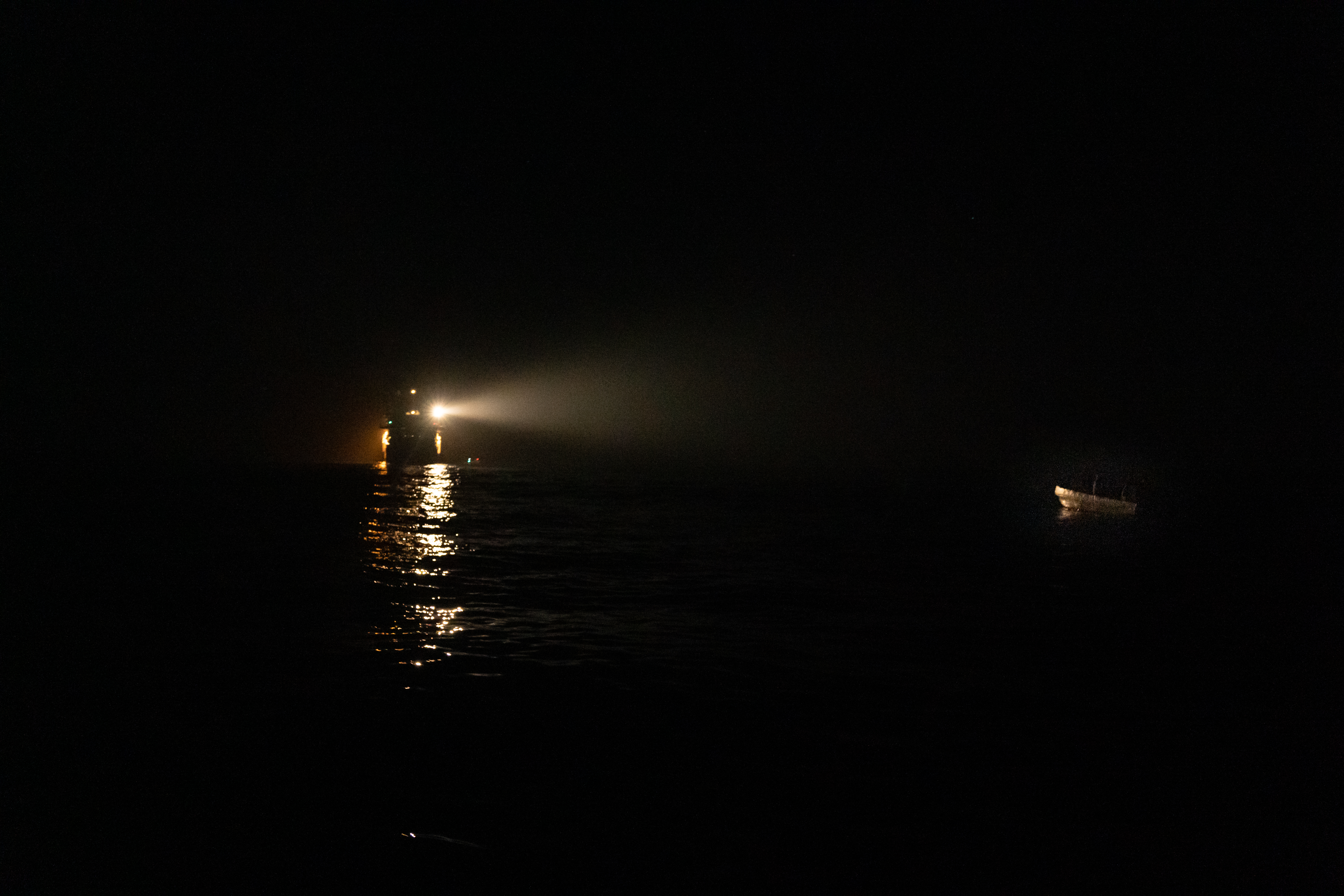 A ship's spotlight reflects on a small boat in distress
