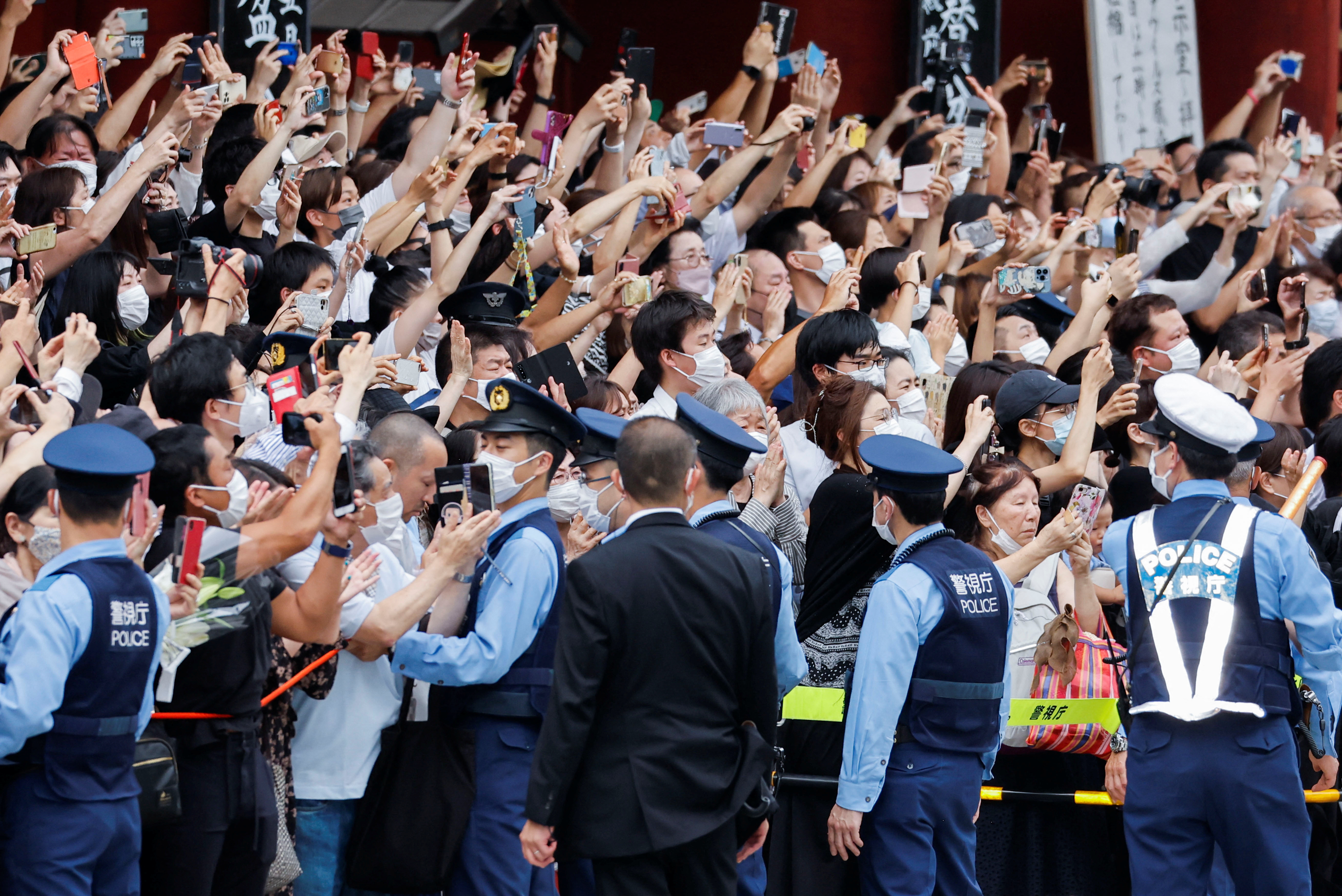 Police officers stand guard as people watch a motorcade with the body of the late former Japanese Prime Minister Shinzo Abe