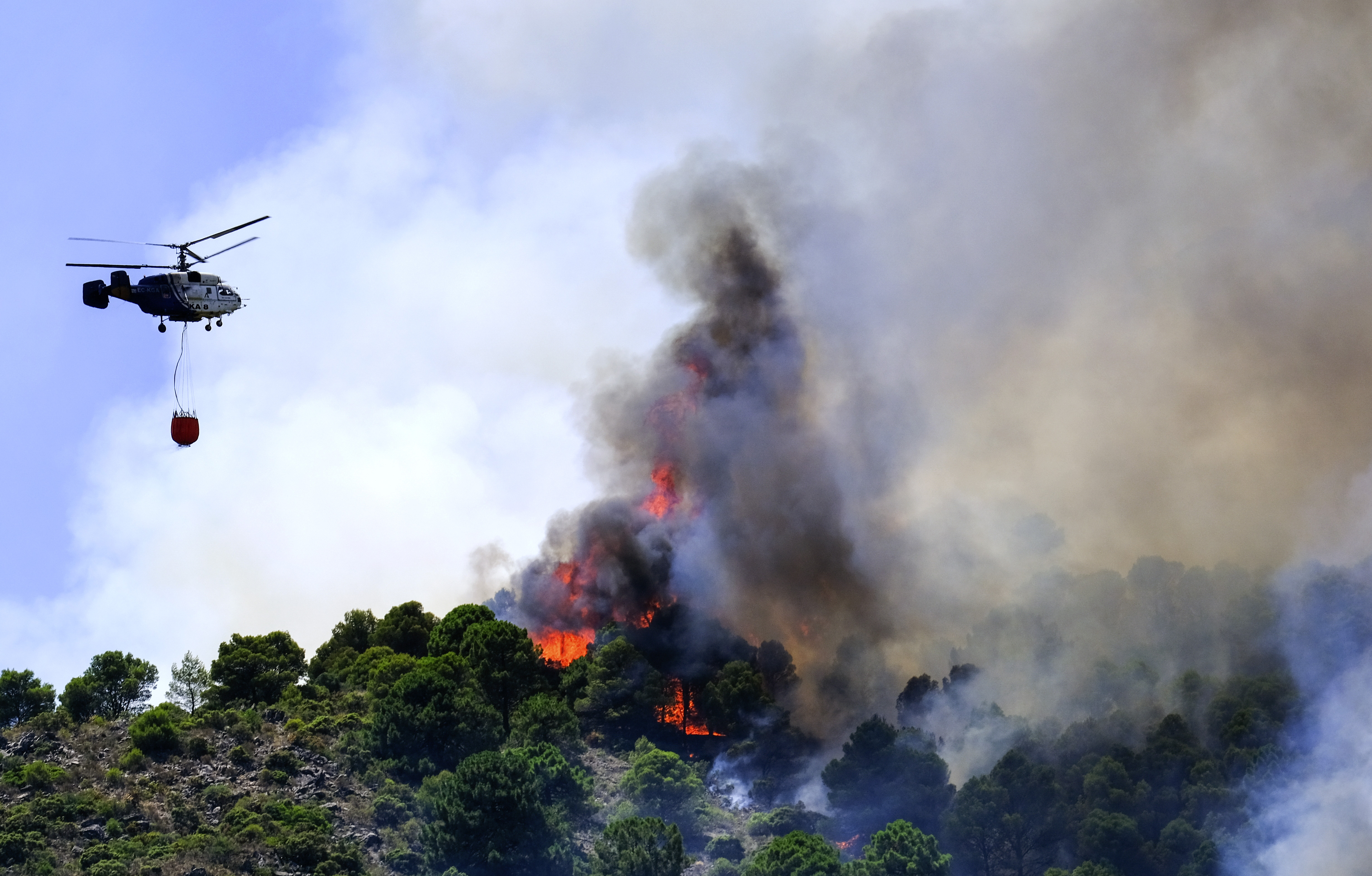 A helicopter launches water as a wildfire advances near a residential area in Alhaurin de la Torre, Malaga, Spain