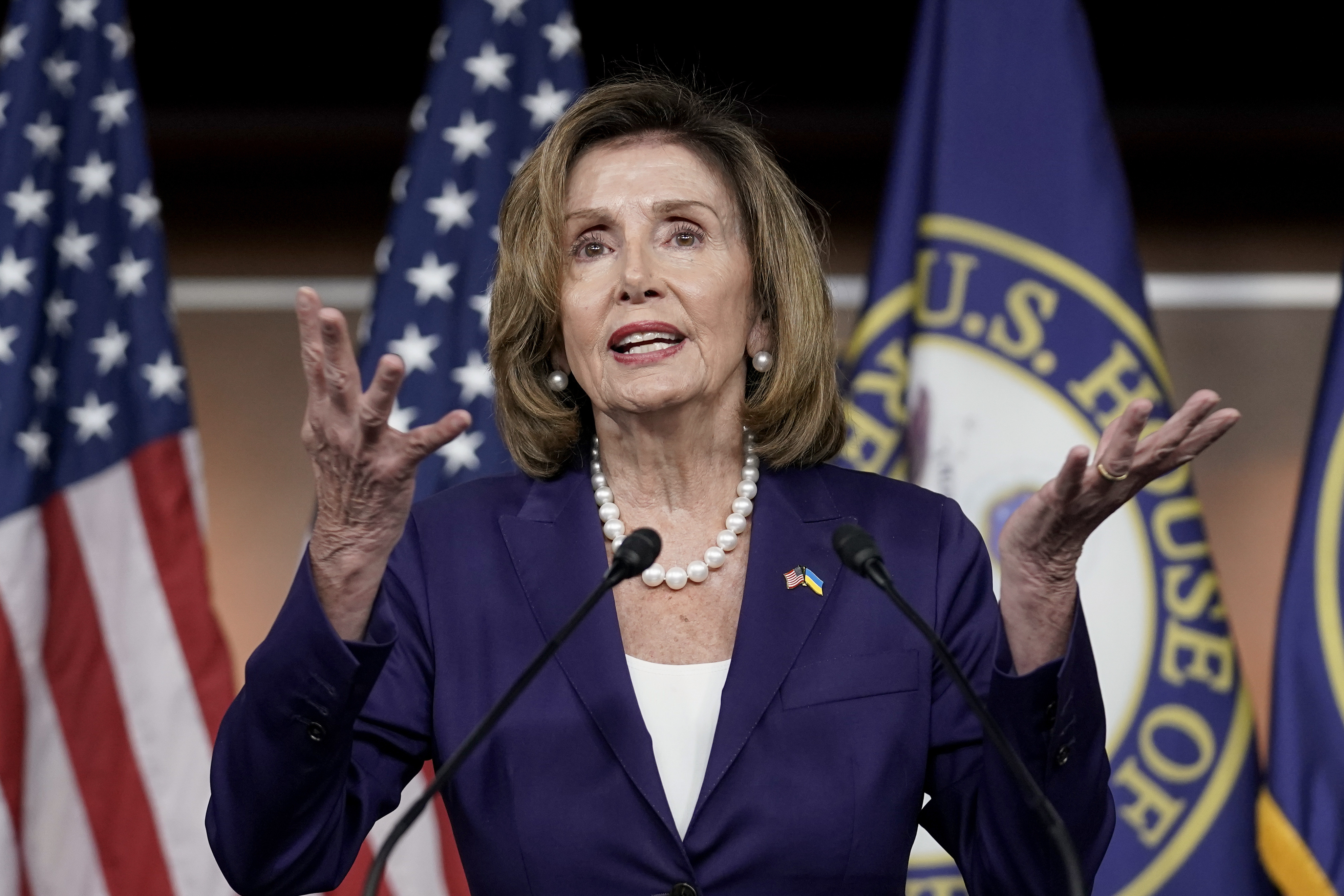 House Speaker Nancy Pelosii, standing in front of a series of US flags, speaks at a press conference