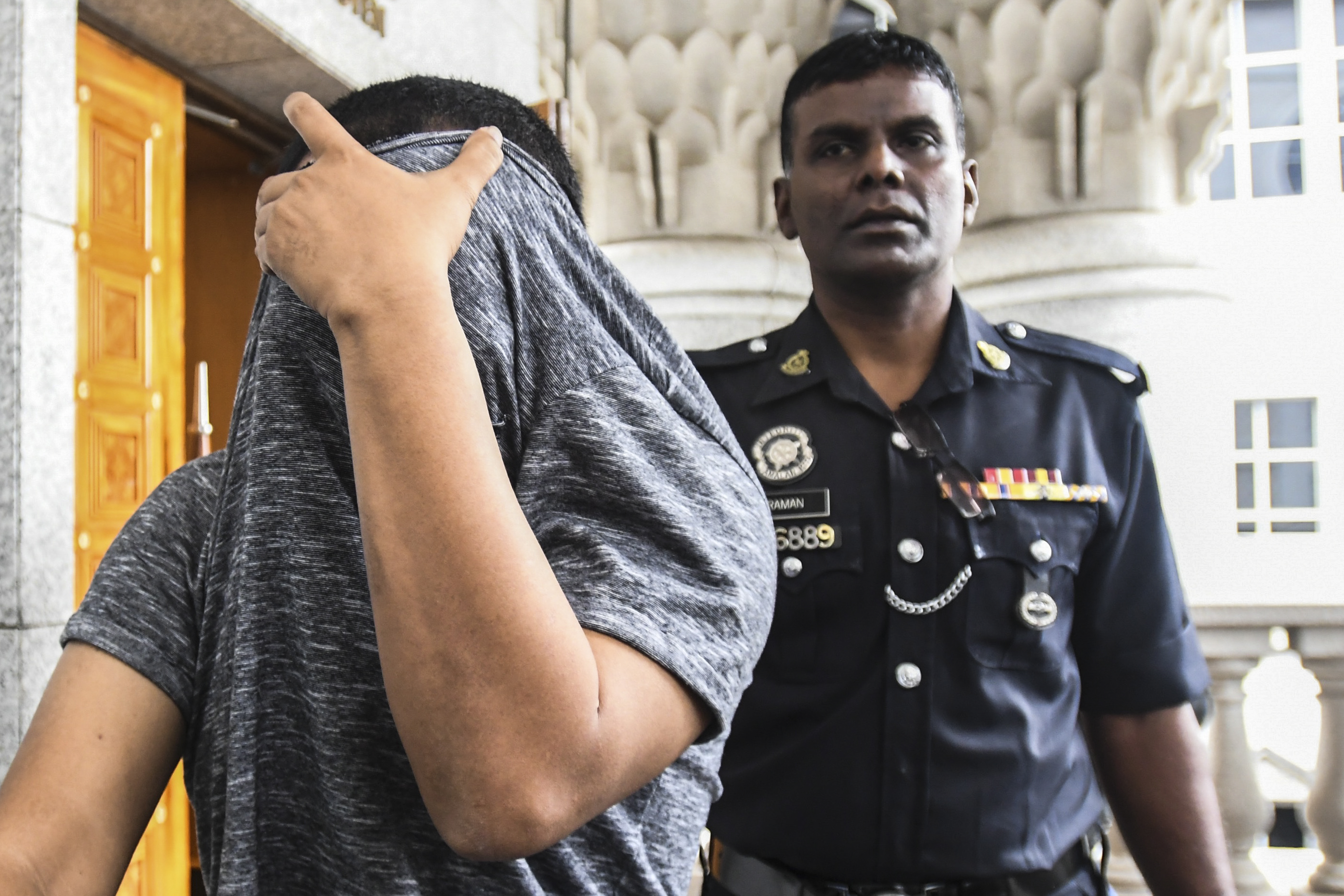 A man accused of sexual assault covers his face as he is escorted by a police officer at a court in Kuala Lumpur