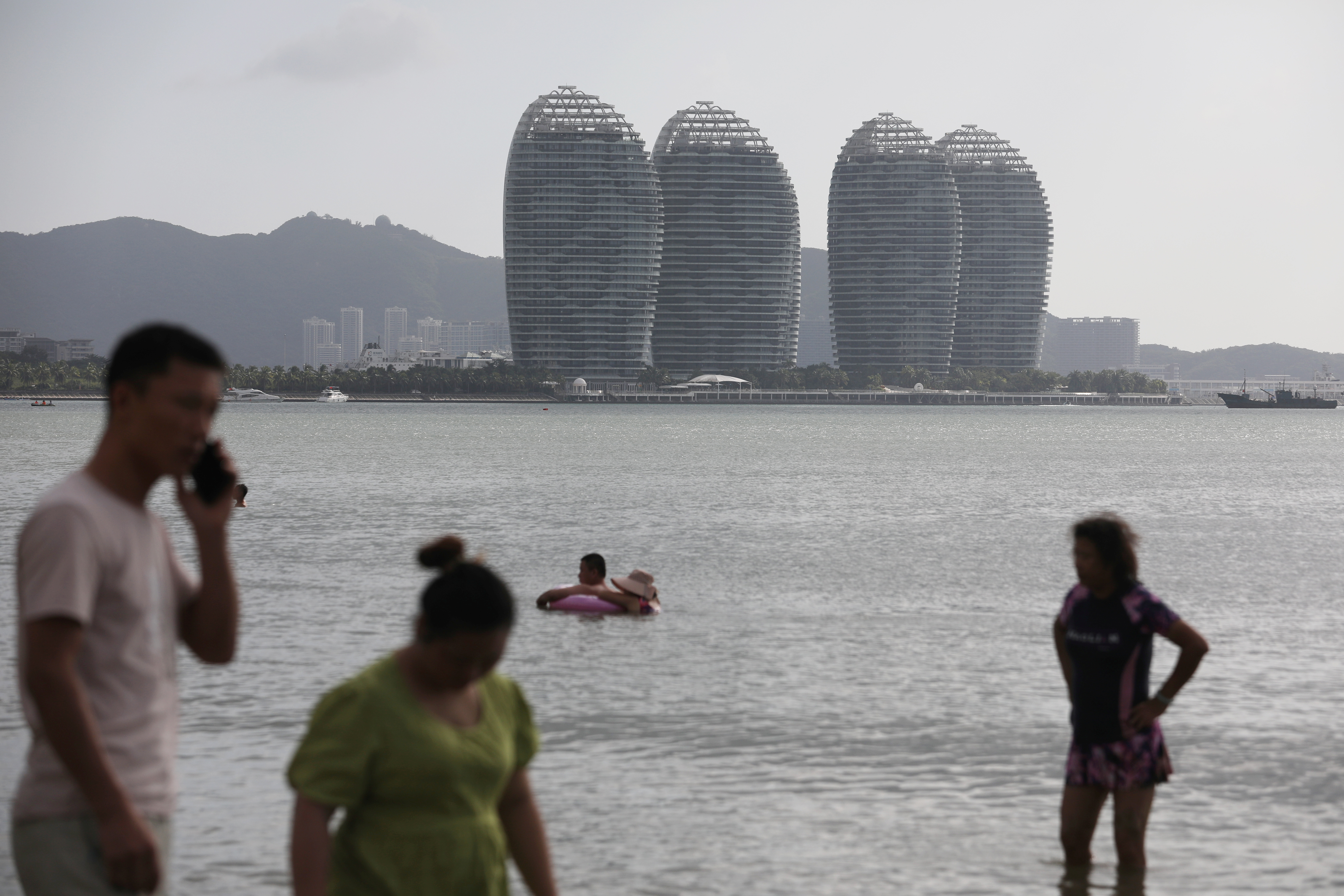 People on Sanya Bay beach against the backdrop of Phoenix Island resort in Sanya, Hainan province, China.