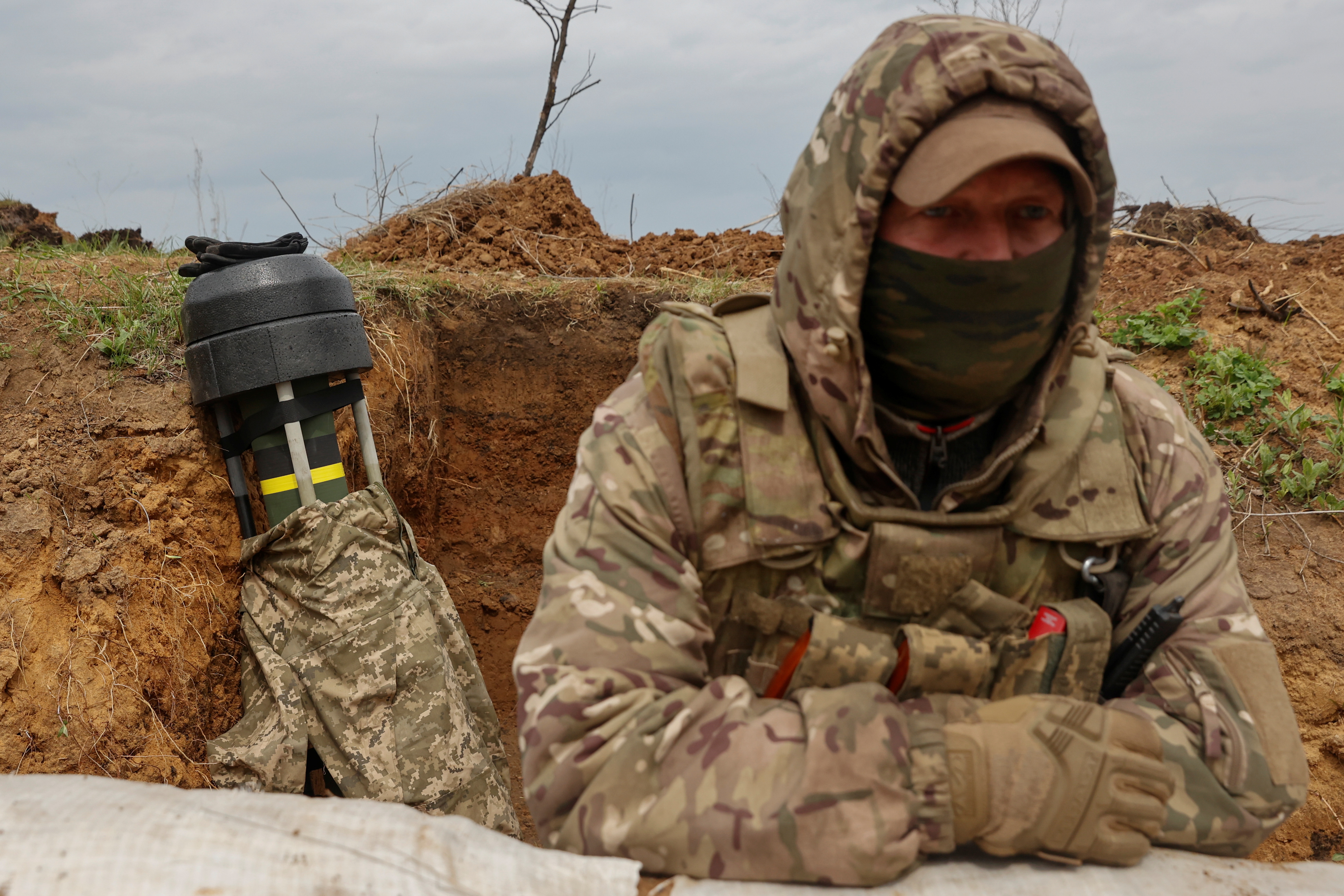 A Ukrainian soldier in camouflage standing in a trench with a Javelin anti-tank missile propped up behind him.