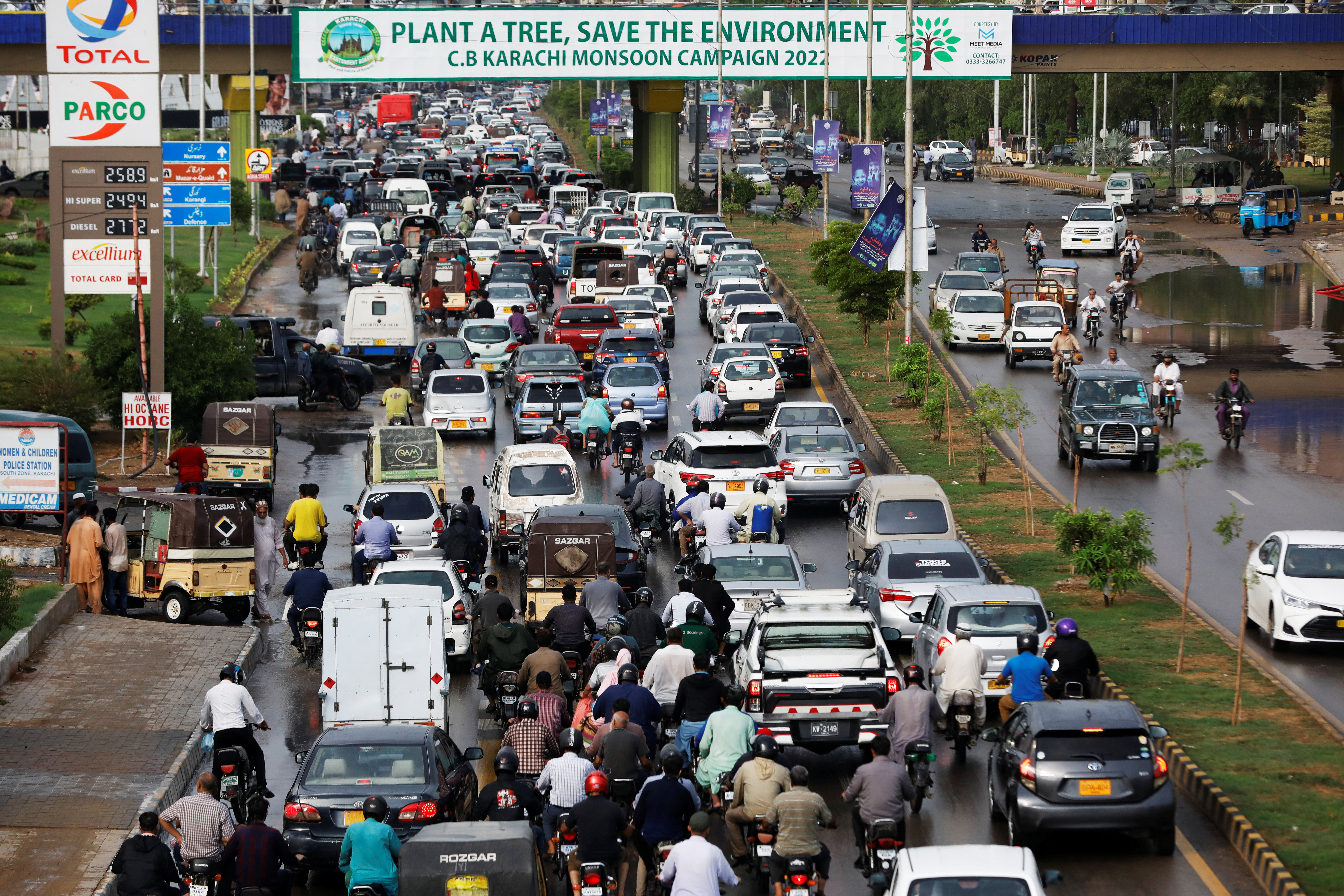 Traffic moves under a bridge displaying a banner from the monsoon tree plantation campaign in Karachi