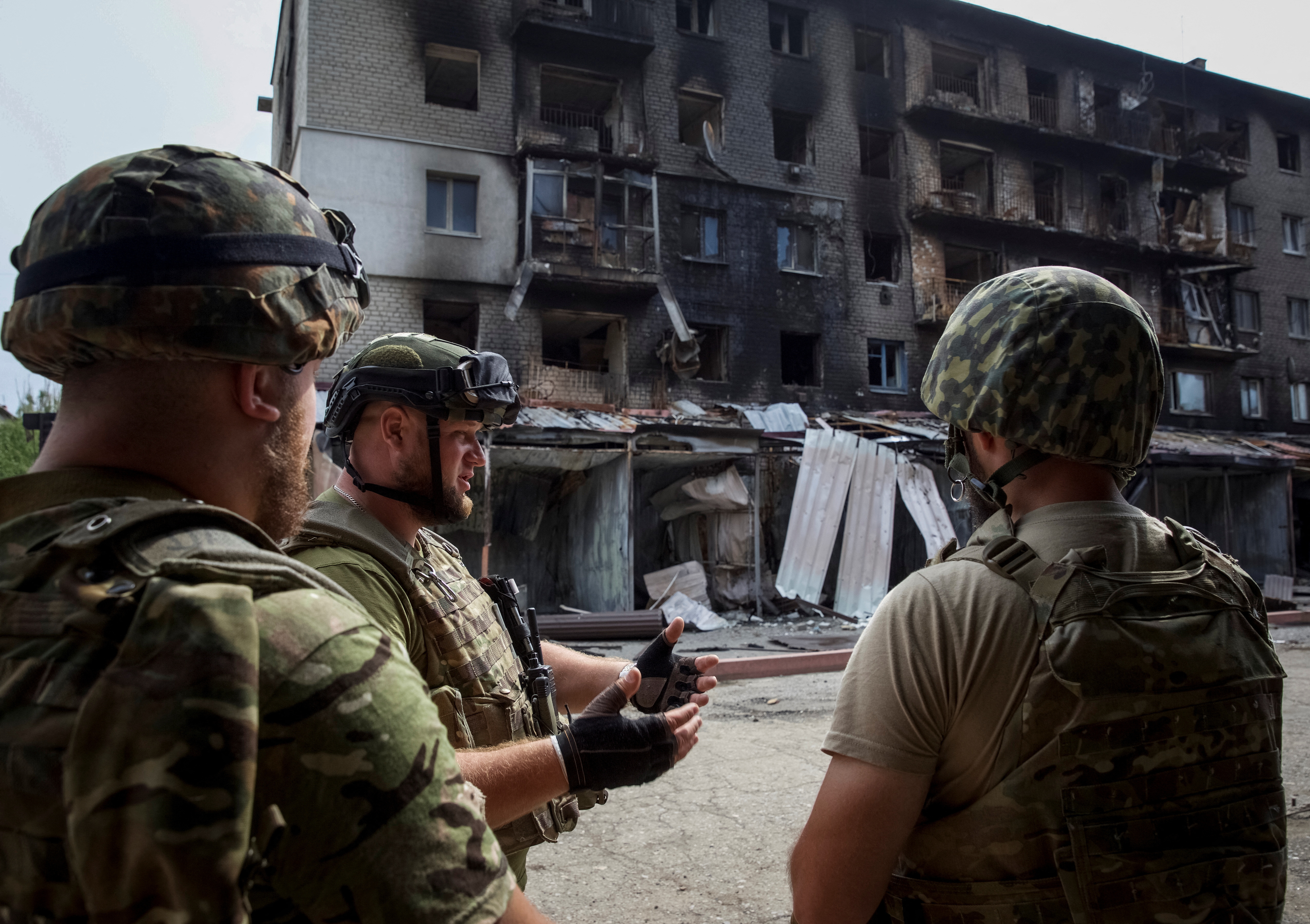 Ukrainian service members speak to each other in front of a residential building damaged by a Russian military raid in the town of Siversk, Ukraine.