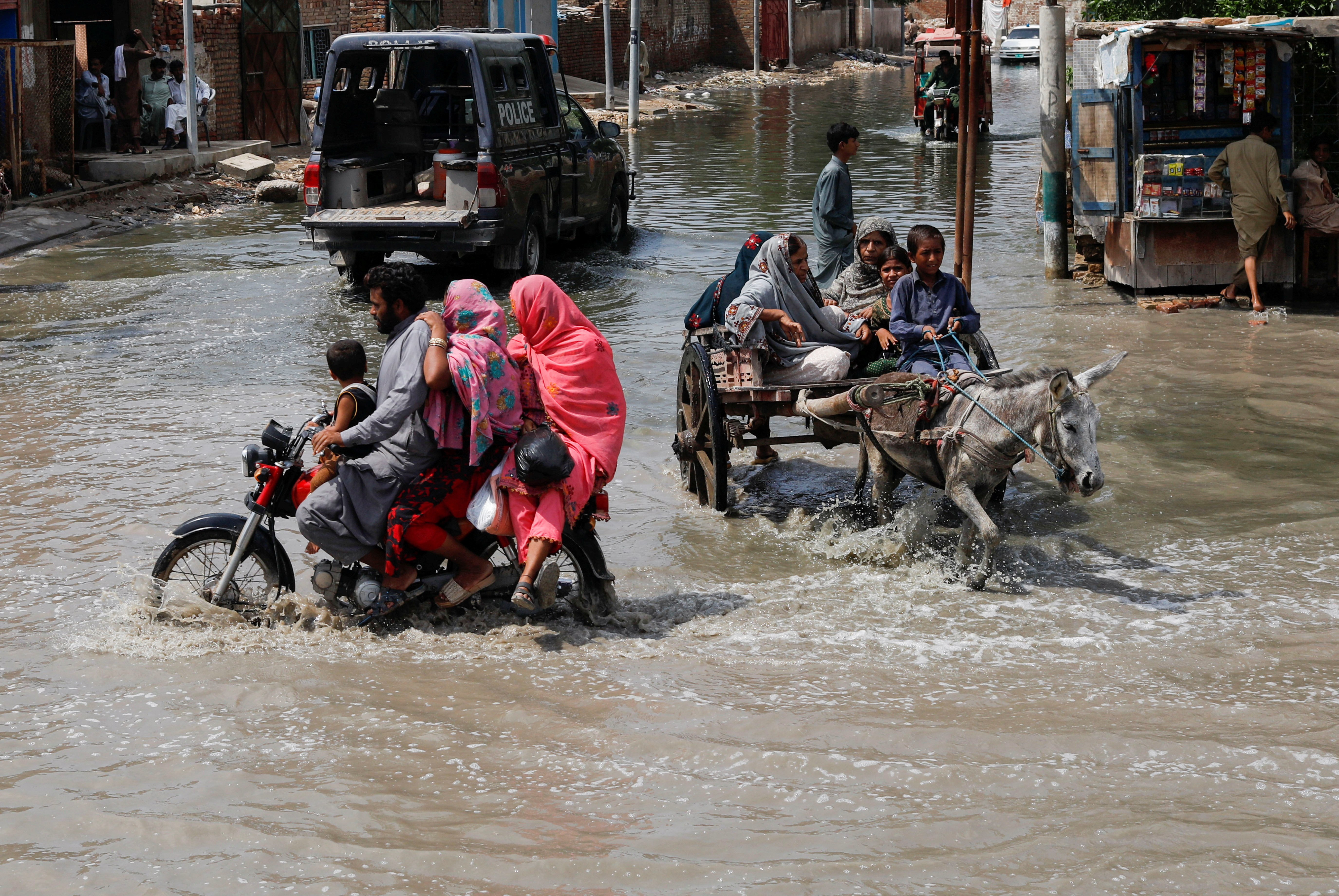 Families travel through water-filled streets on motorcycle and on a donkey cart in Jacobabad, Pakistan.