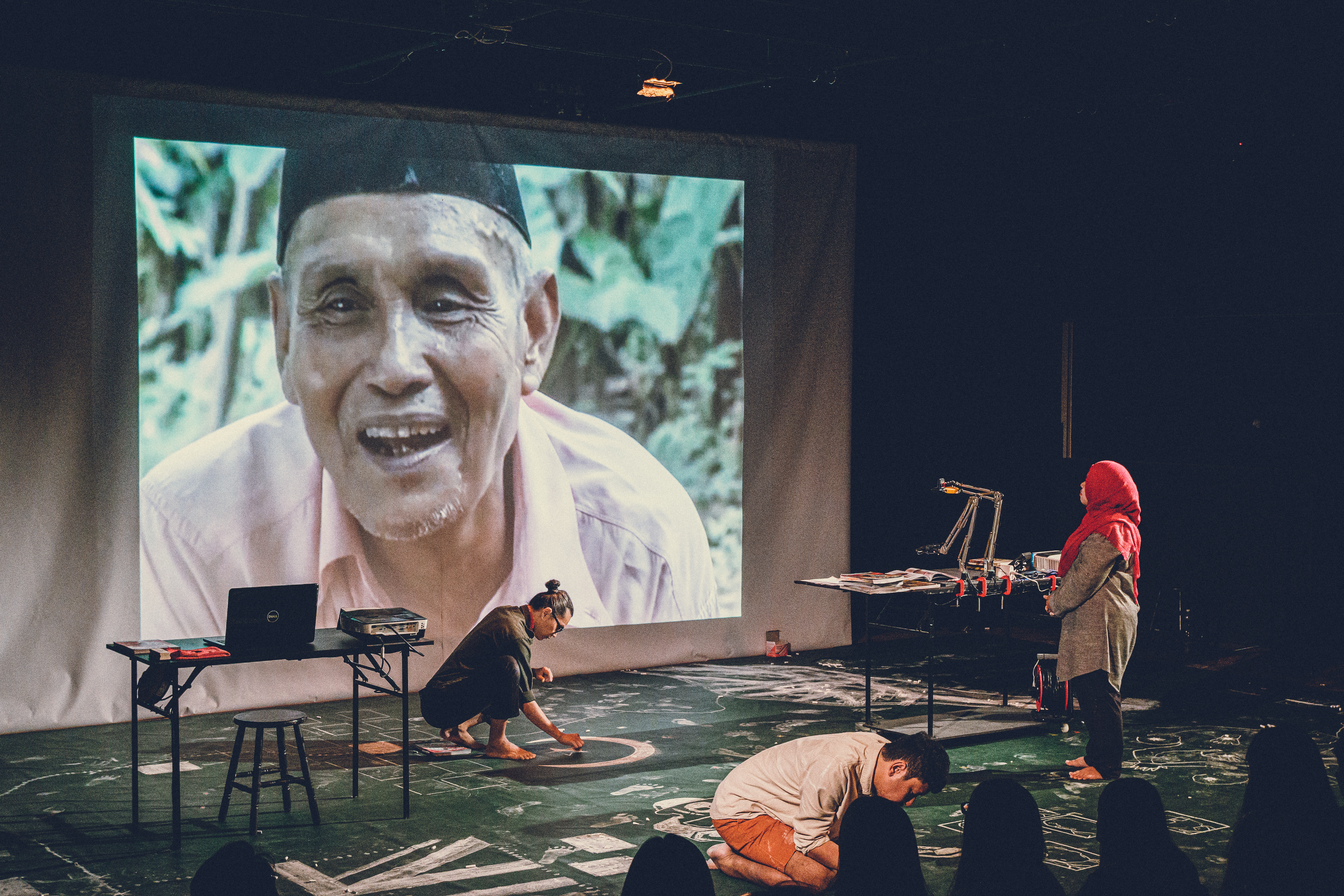 A video of an interview with an exiled communist revolutionary plays behind a performer in A Notional History