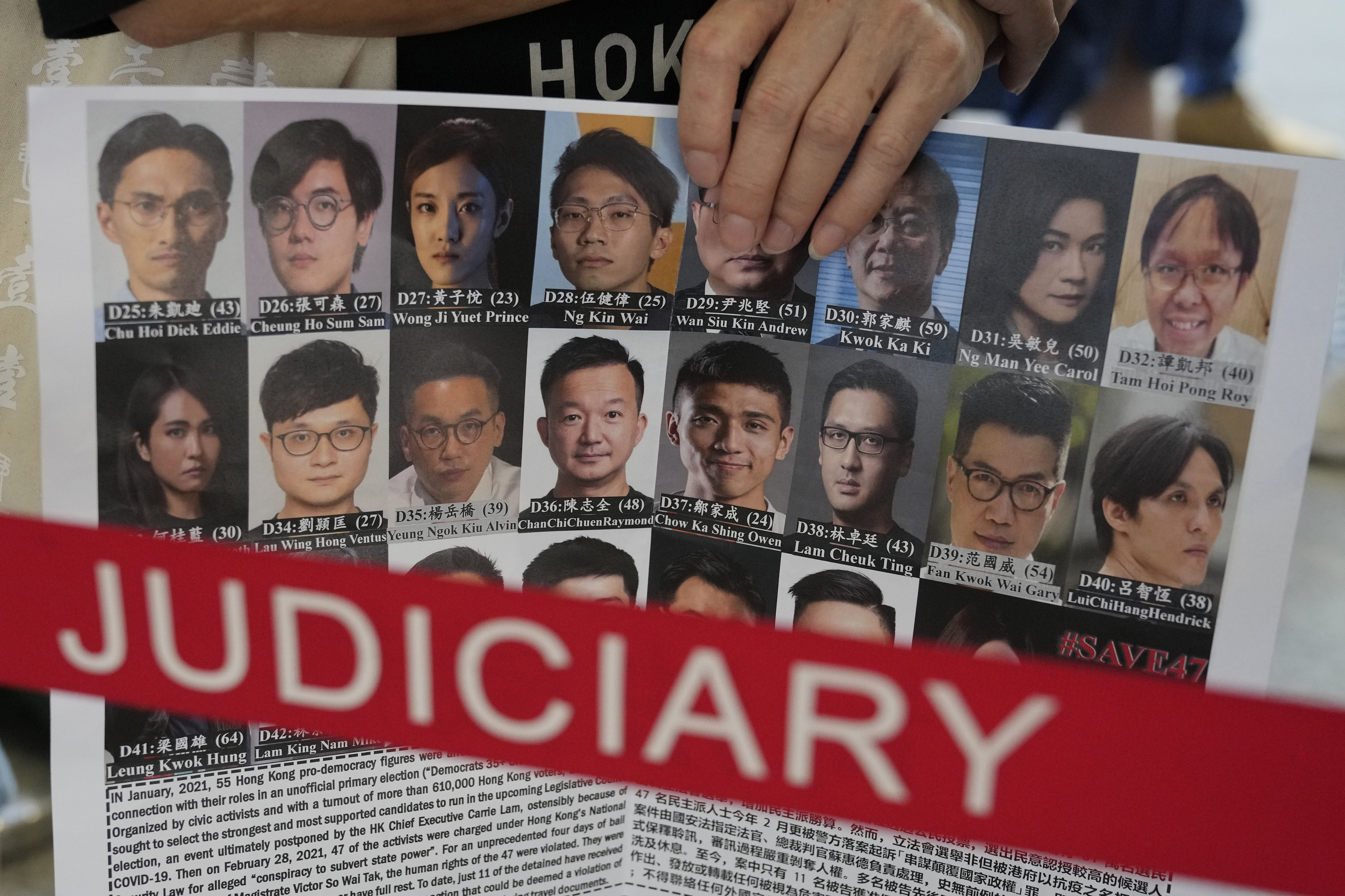 A person standing outside a court in Hong Kong carries a poster showing the 47 pro-democracy politicians and activists arrested for organising a primary to choose their own candidates for an election that was then postponed
