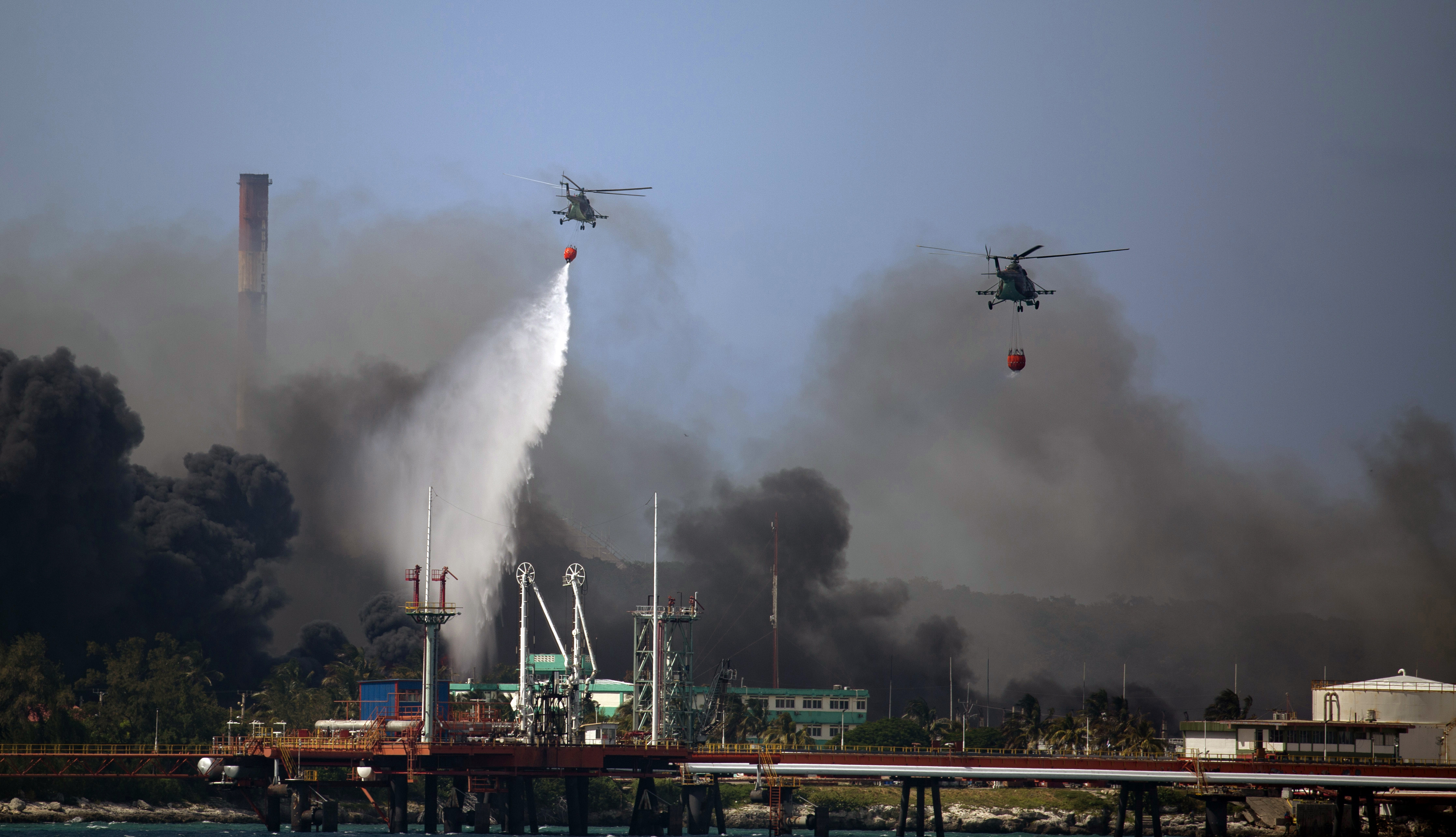 Helicopters hauling water fly over the Matanzas Supertanker Base, as firefighters and specialists work to quell the blaze which began during a thunderstorm in Matanzas, Cuba