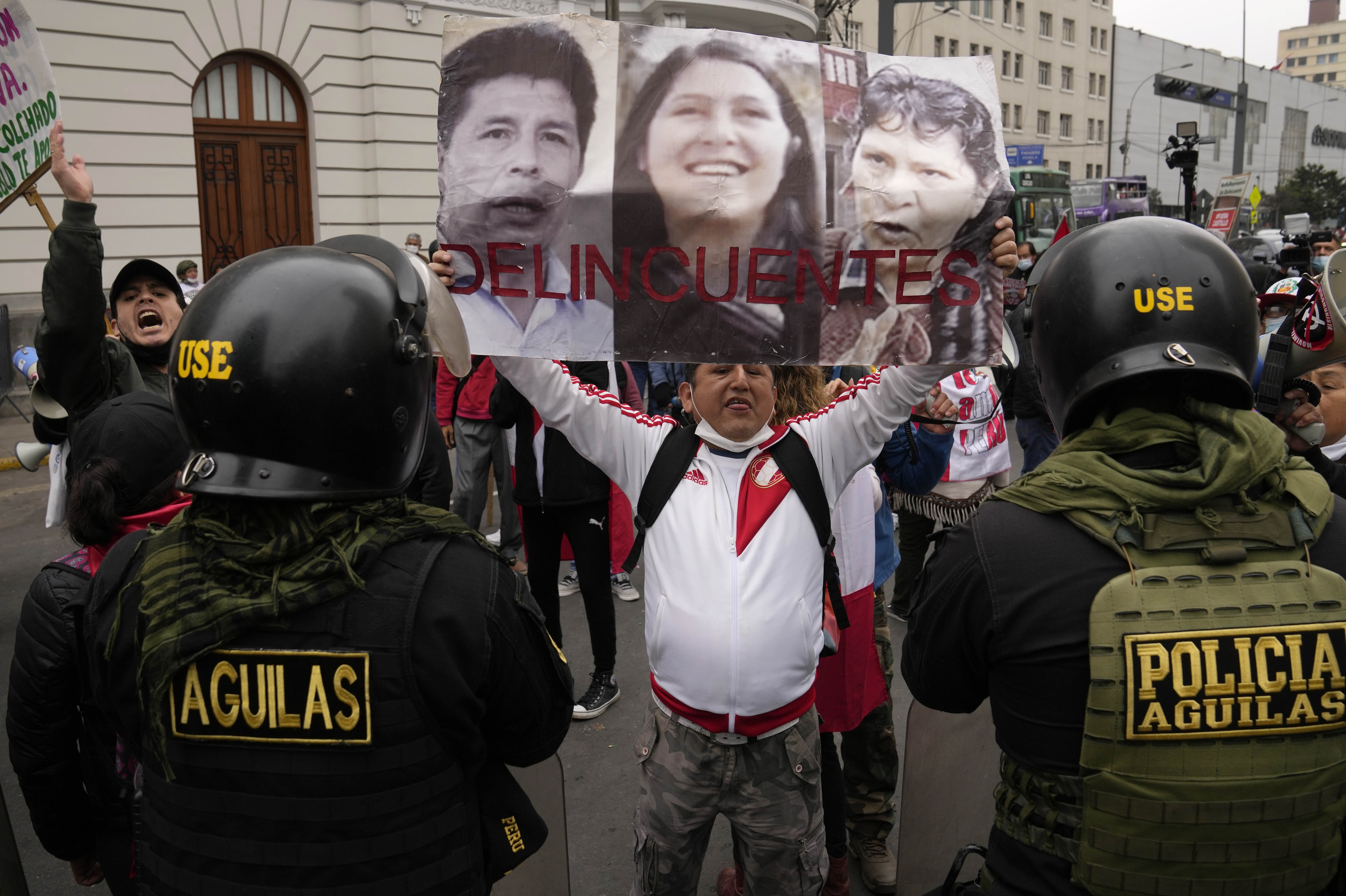 An opponent of the government of President Pedro Castillo holds photos of Castillo, his sister-in-law Yenifer and his wife Lilia Paredes with text that reads in Spanish, "Criminals".
