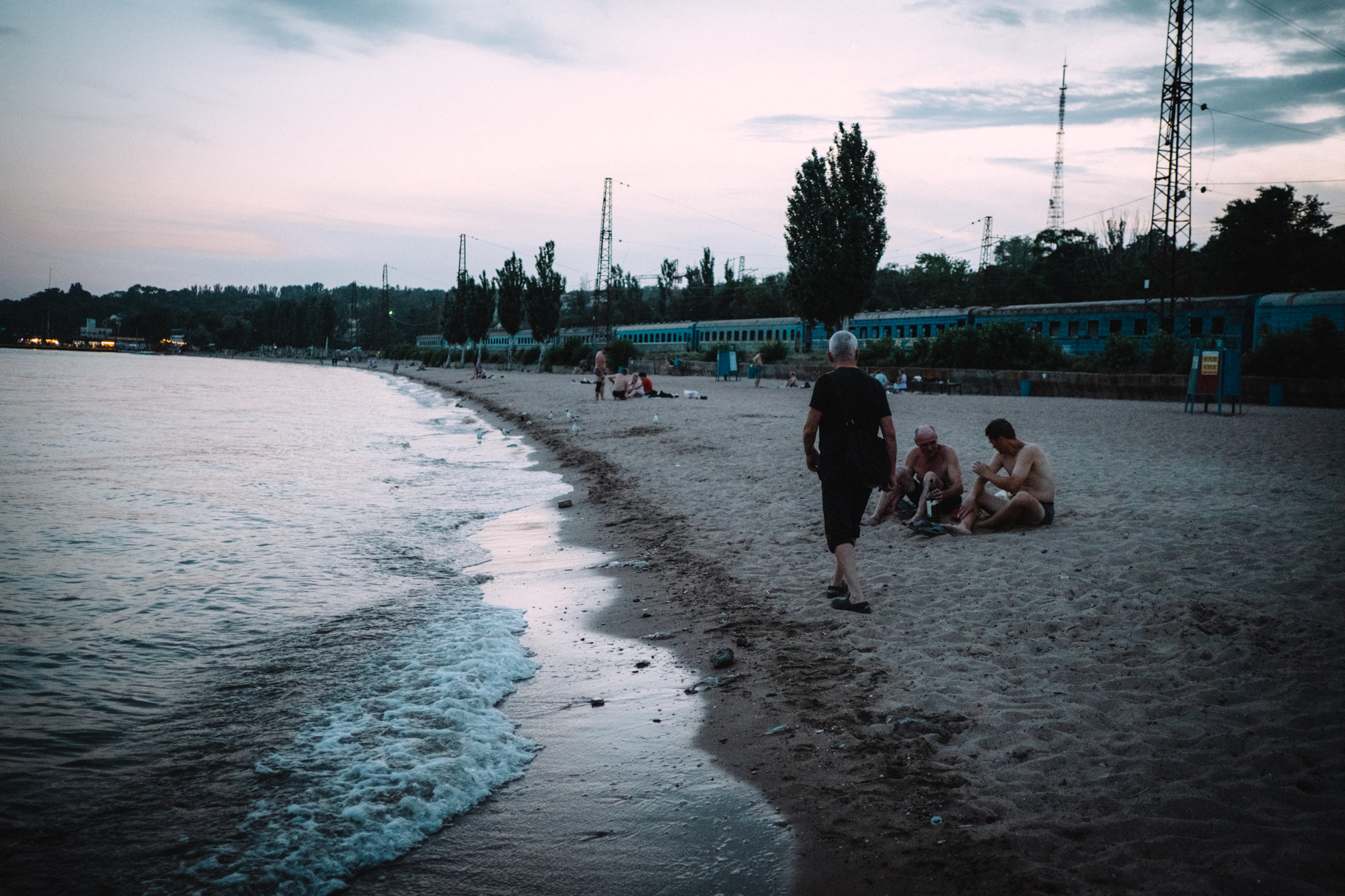 A photo of a shoreline with a few people sitting on the sand on the beach.