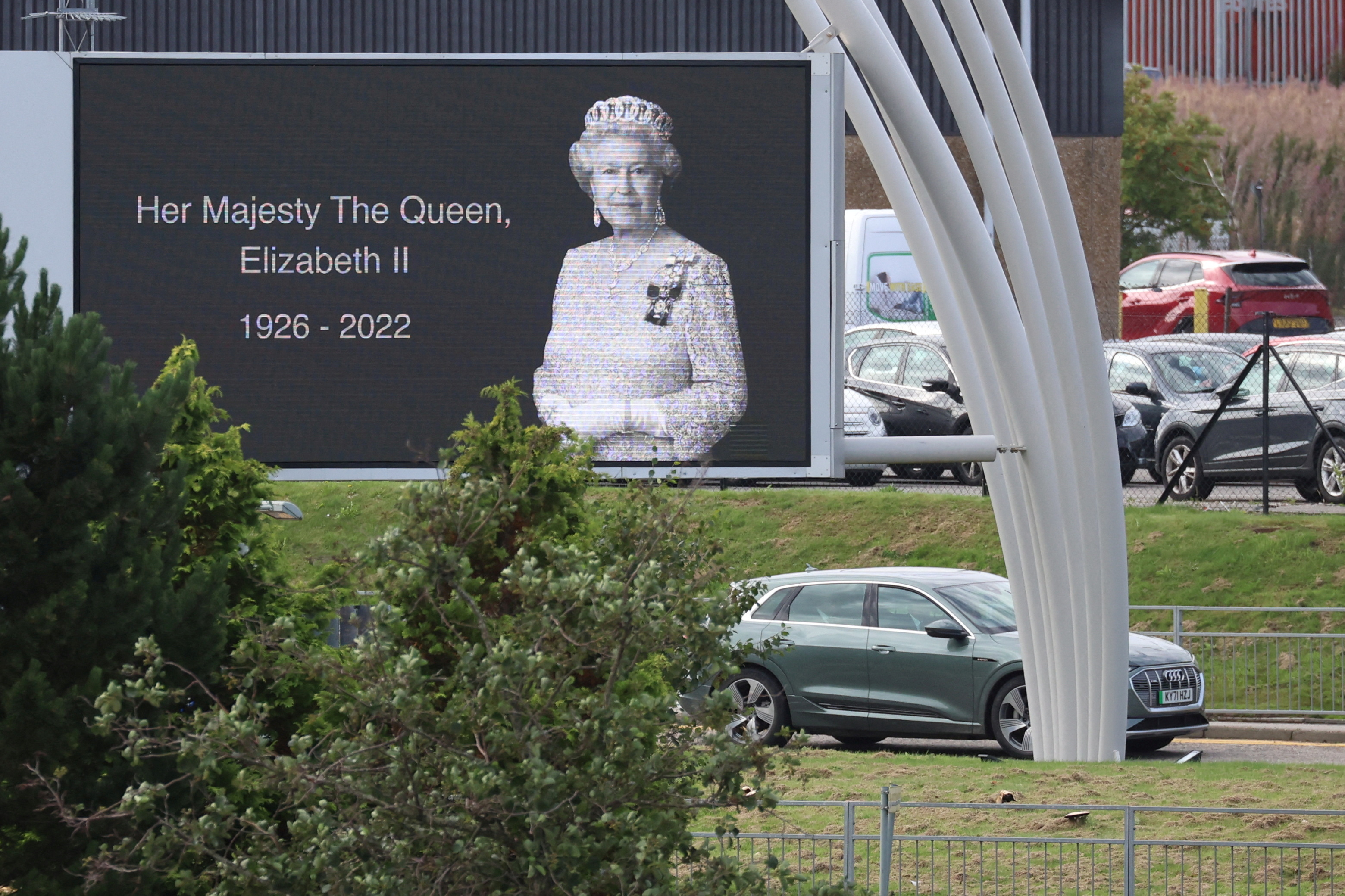 A car carrying Britain's King Charles and Queen Camilla drives past a poster of late Queen Elizabeth outside Aberdeen International Airport to fly to London, following the passing of Britain's Queen Elizabeth, in Aberdeen, Britain, September 9, 2022. REUTERS/Phil Noble