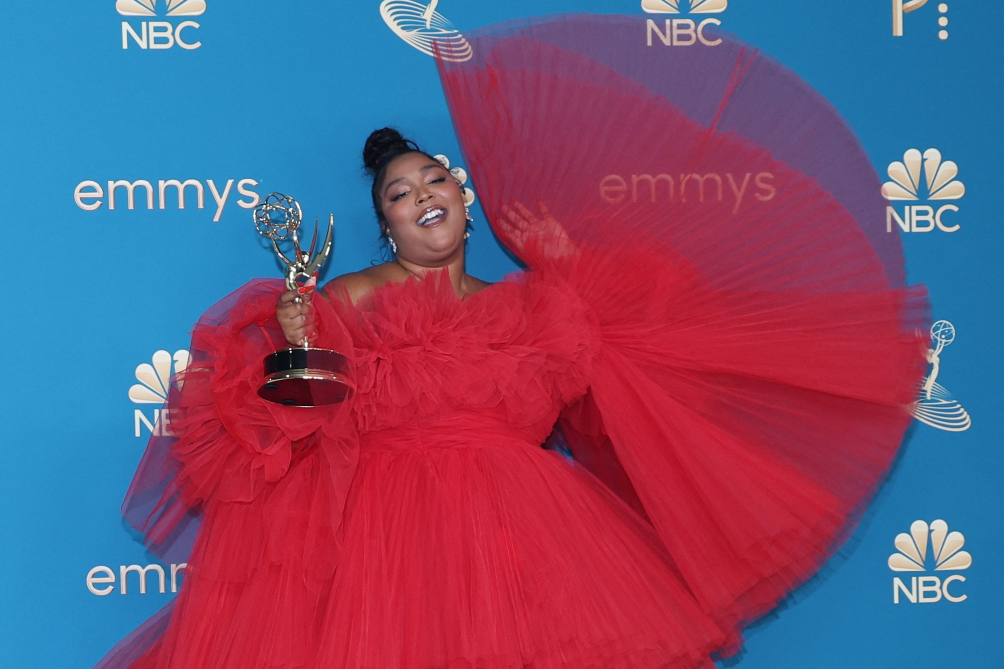 Lizzo, in a red dress, holds her Emmy