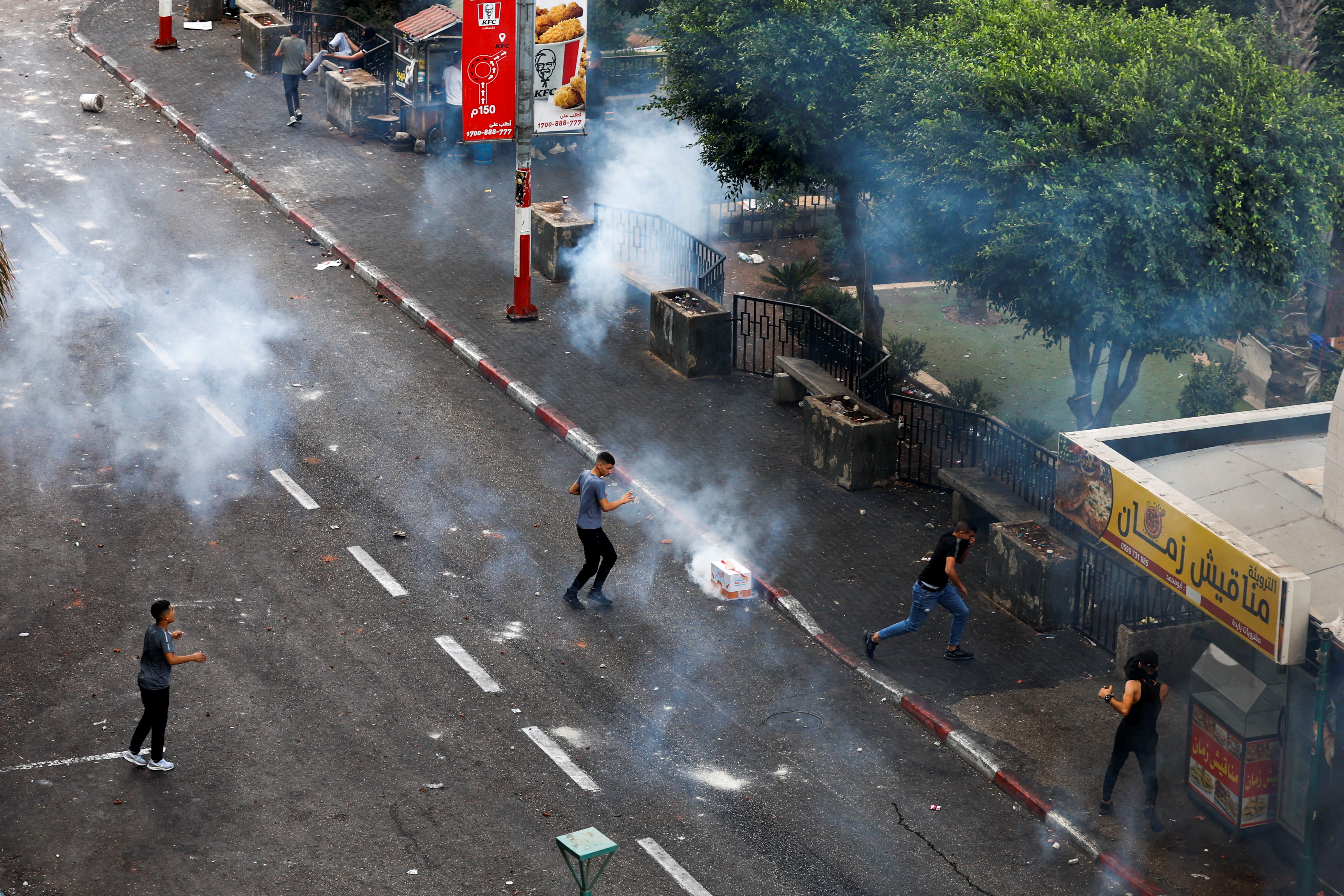 Palestinian men in a street as tear gas explodes around them