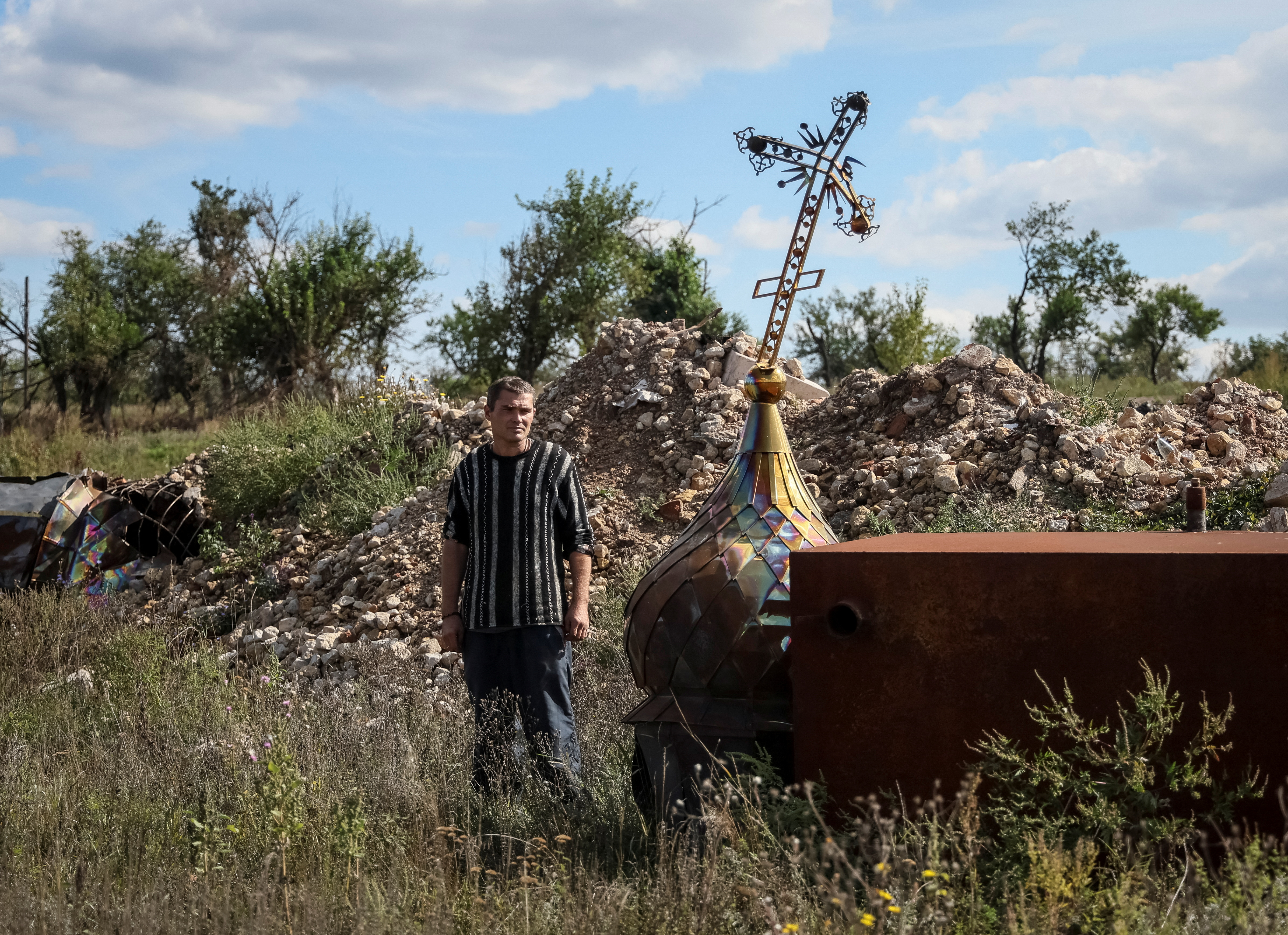 Local resident Yuriy Zdorovets, 42, looks at a cross from a destroyed church in the village of Kamyanka, recently liberated by Ukrainian Armed Forces, in Kharkiv region, Ukraine September 22, 2022. REUTERS/Gleb Garanich