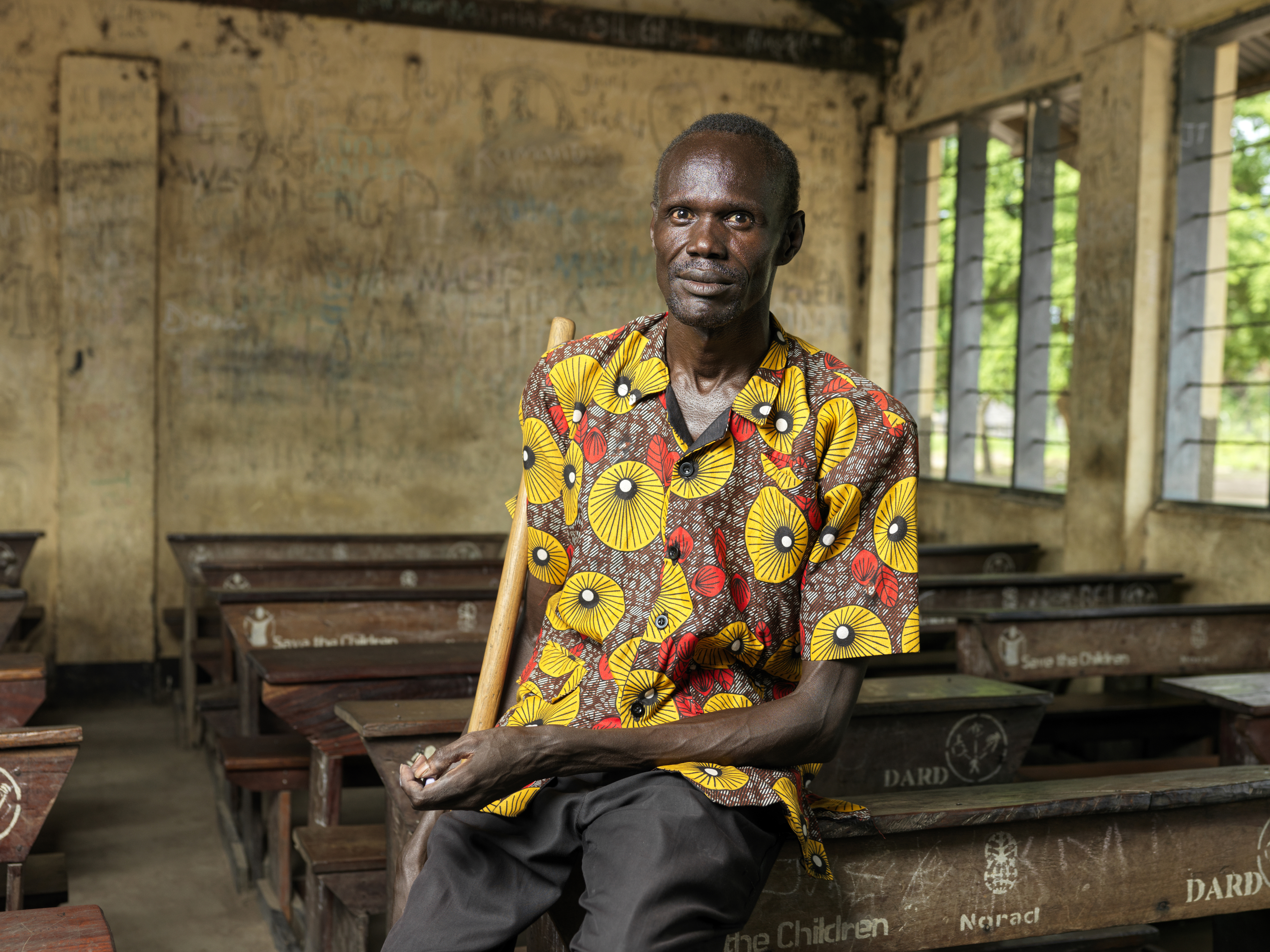 A photo of Clement Makuak sitting on a desk in an empty classroom.