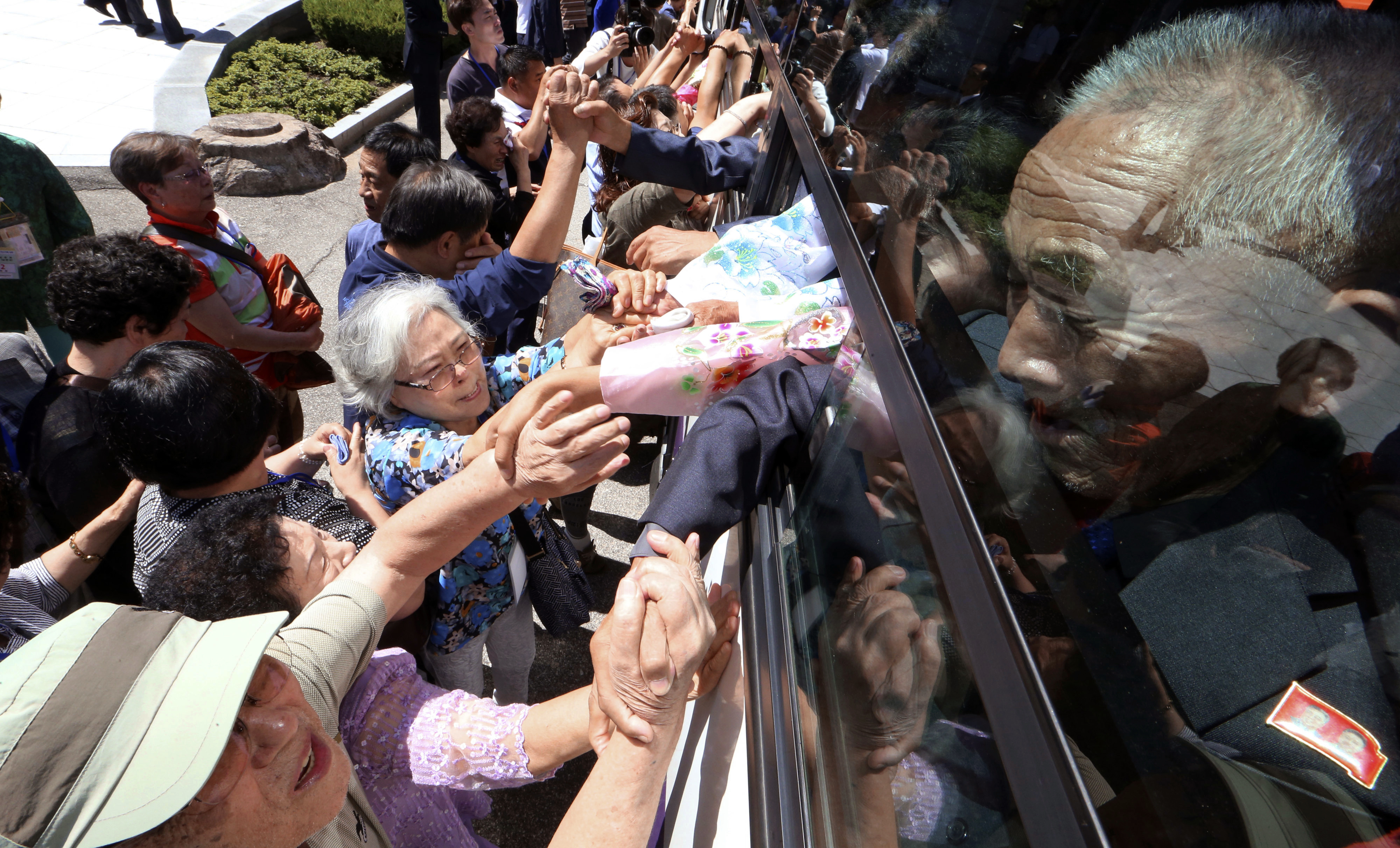 Elderly North Koreans, their faces anguished and some crying, stretch out their hands to grasp those of their relatives in South Korea as they leave on a bus