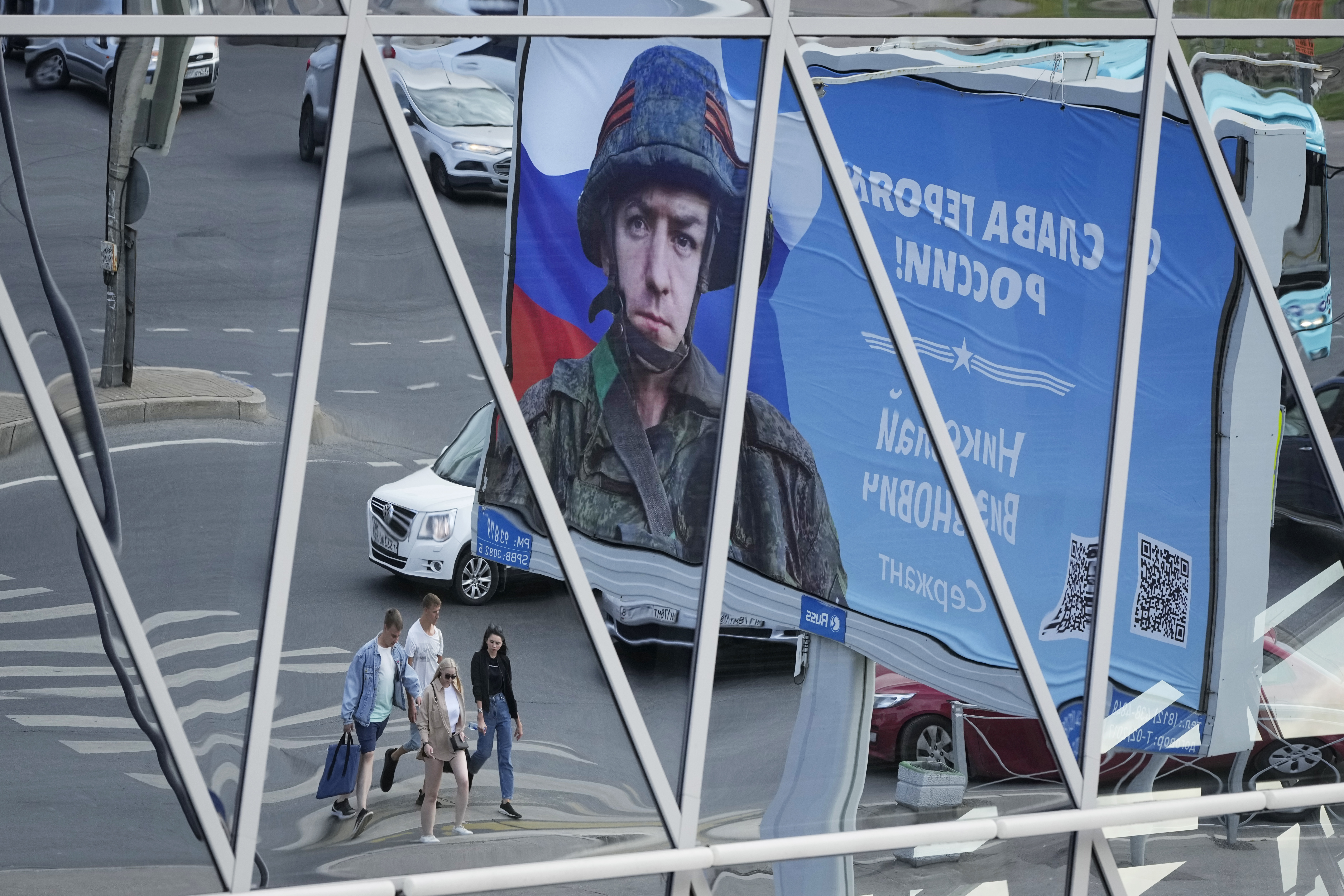 A billboard with a portrait of a Russian soldier and the words "Glory to the heroes of Russia" is reflected in a shopping mall in St. Petersburg