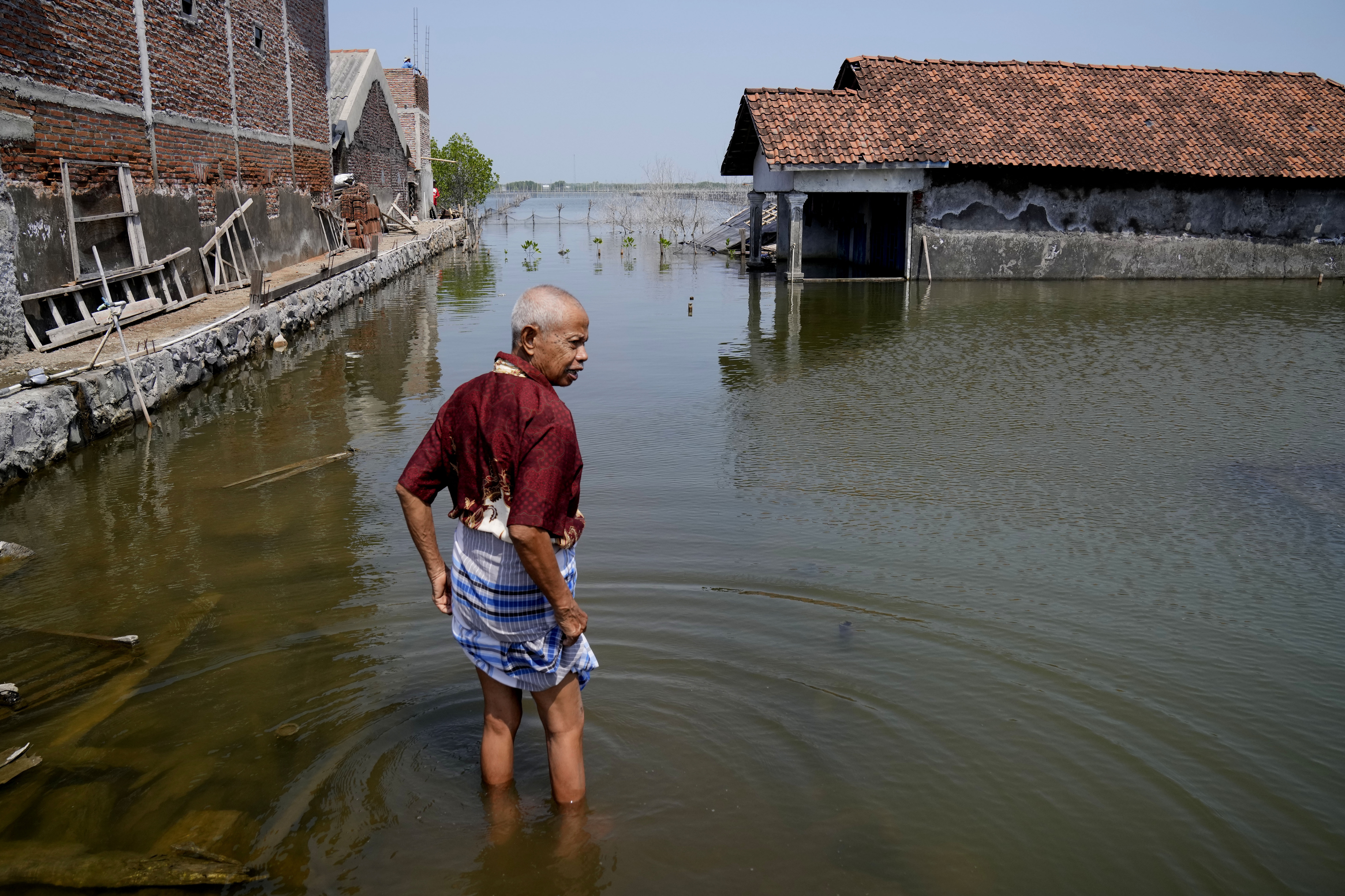 Sukarman walks on a flooded pathway outside his house
