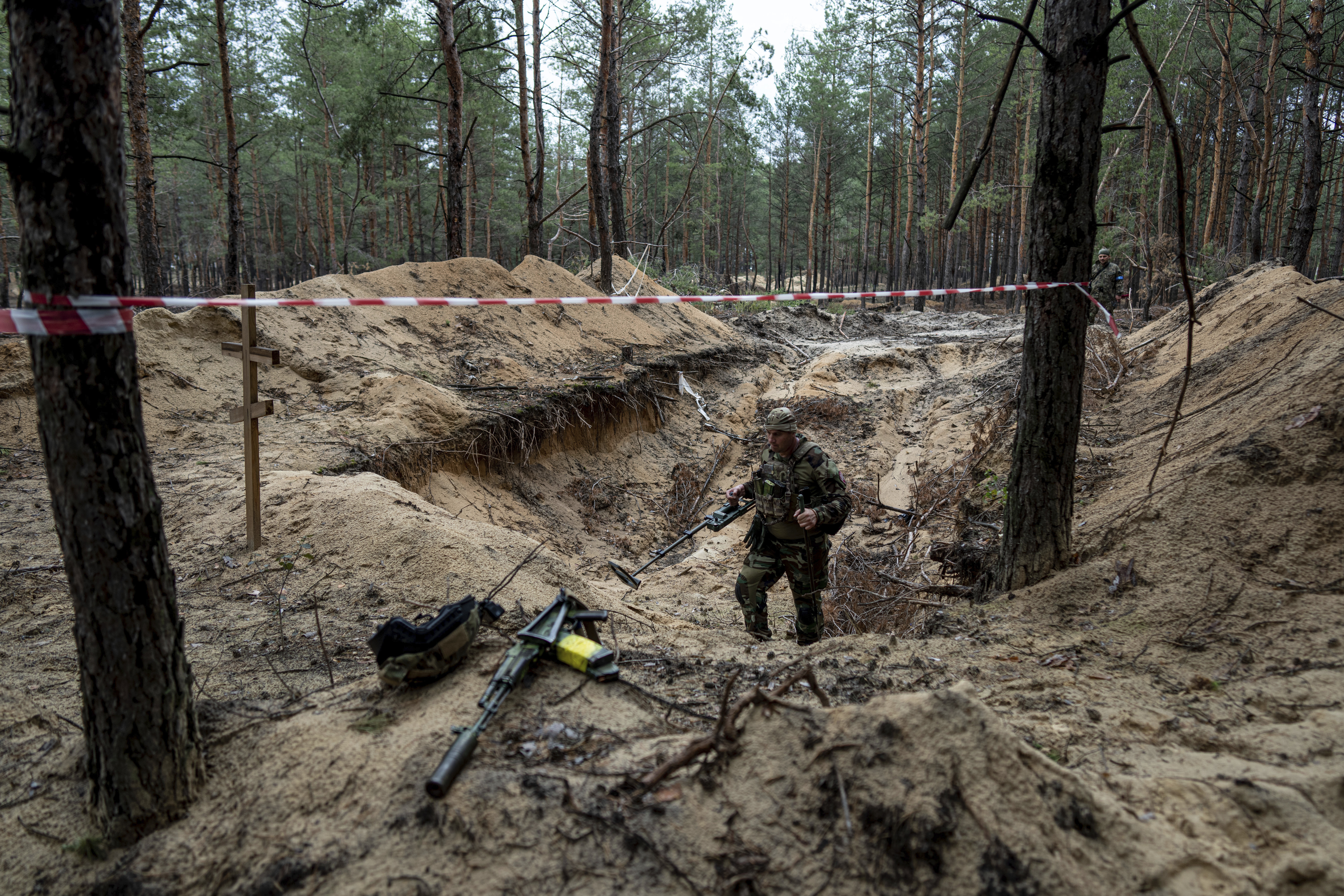 A soldier stands in the mud surrounded by trees where a mass grave was discovered near Izyum, Ukraine.