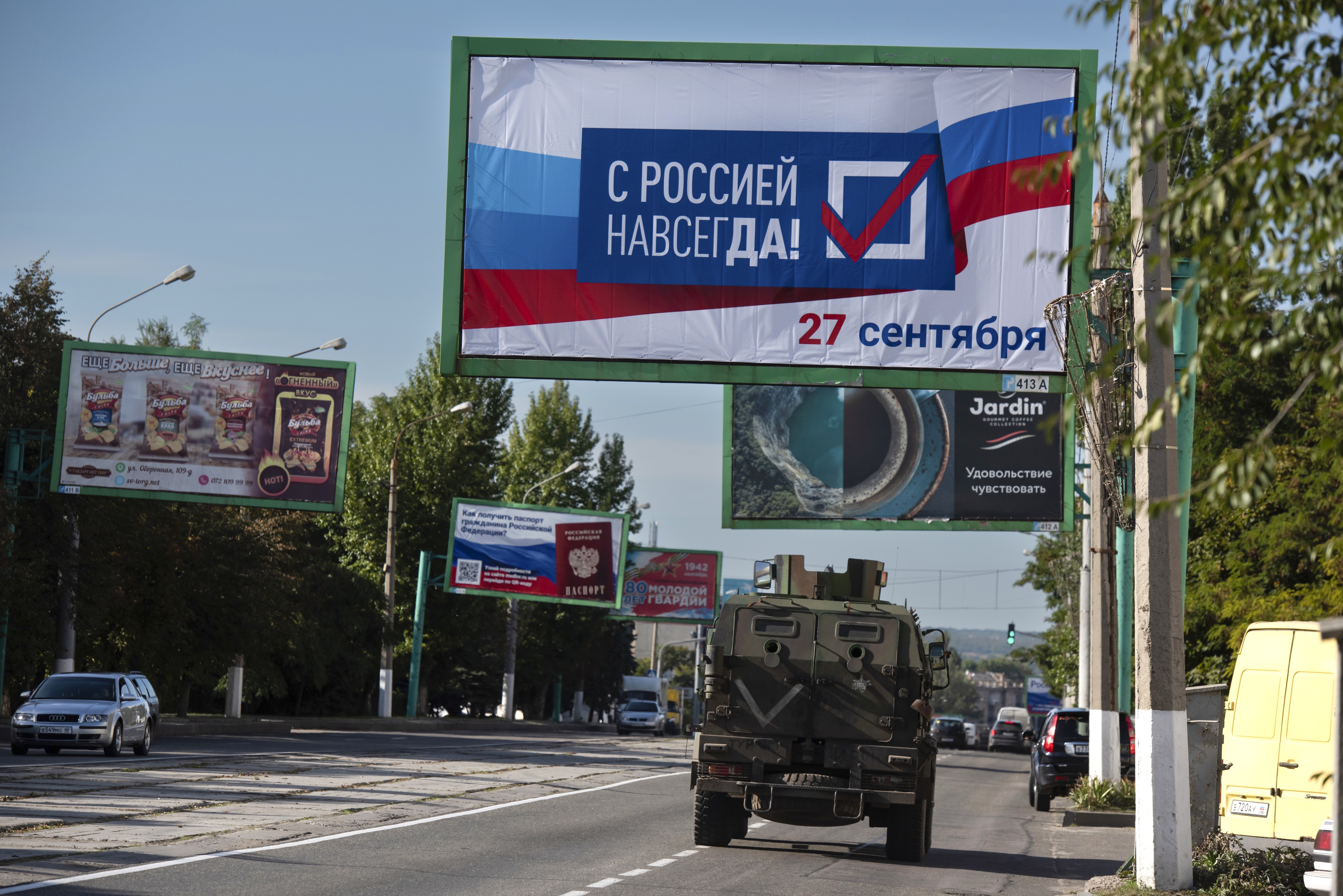 A military vehicle drives along a street with a billboard that reads: "With Russia forever, September 27", ahead of a referendum in Luhansk